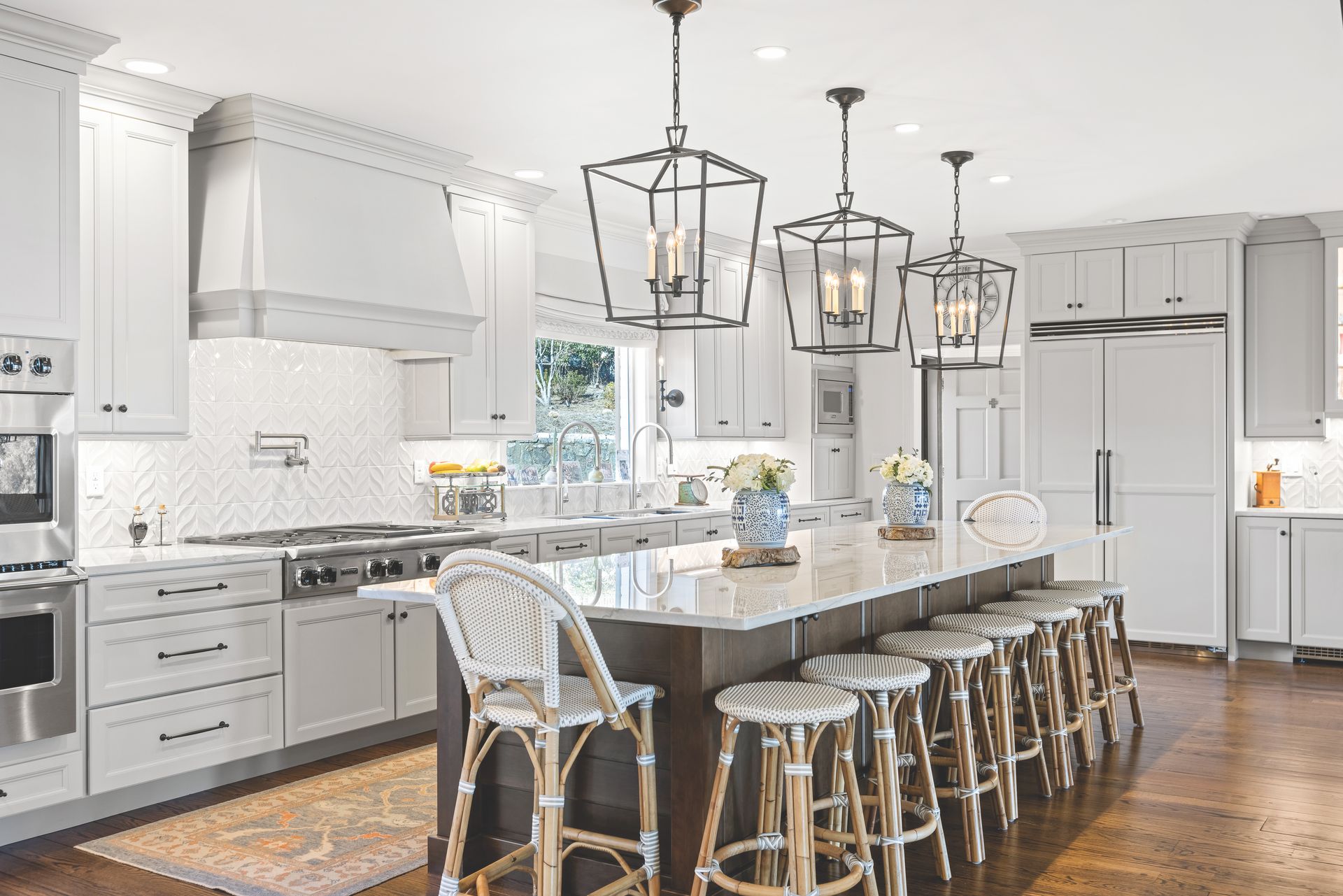 Elegant white kitchen with a large island, stools, and pendant lights.