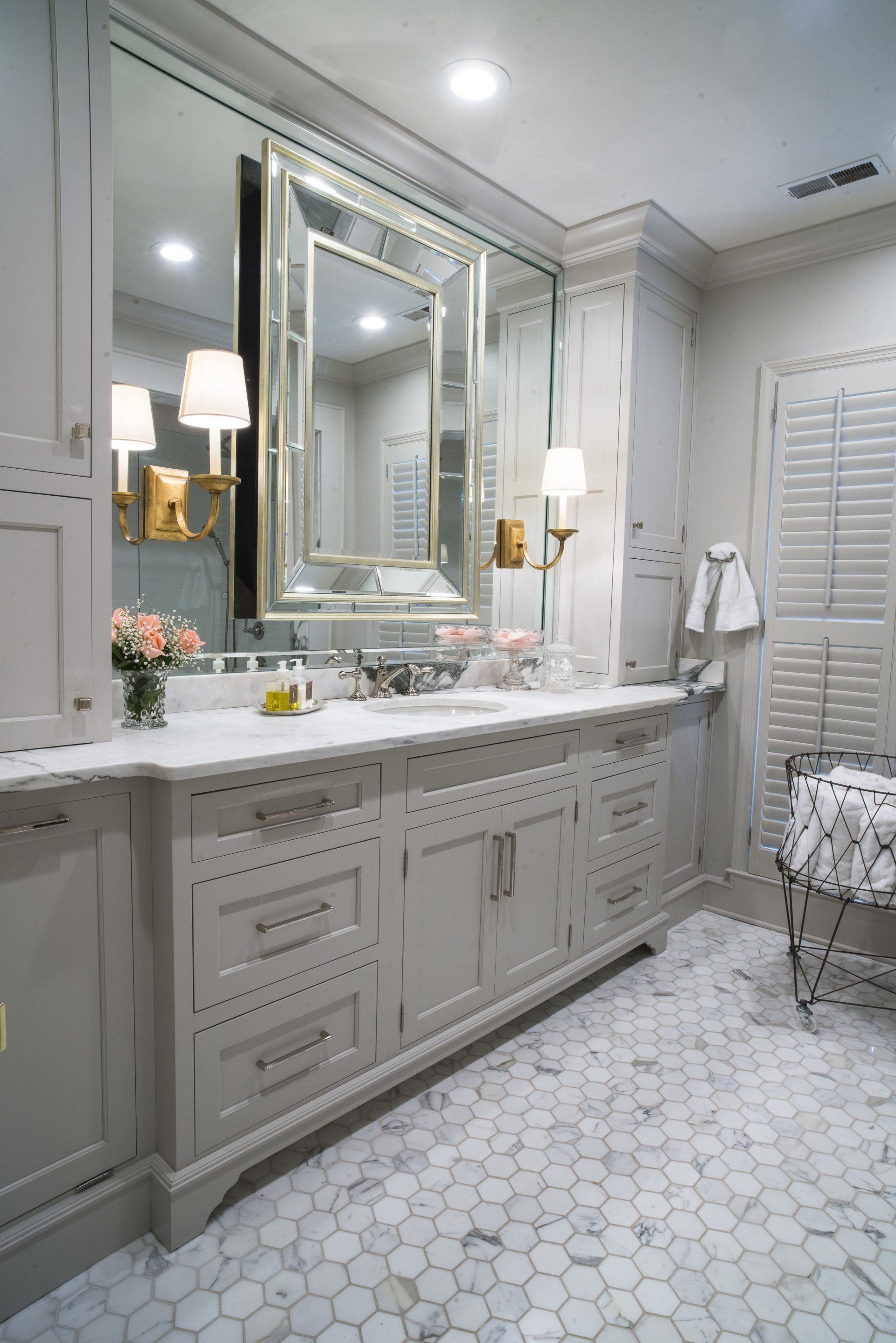 Bathroom with light gray cabinets, marble countertops, and a large framed mirror. Hexagon tile floor.