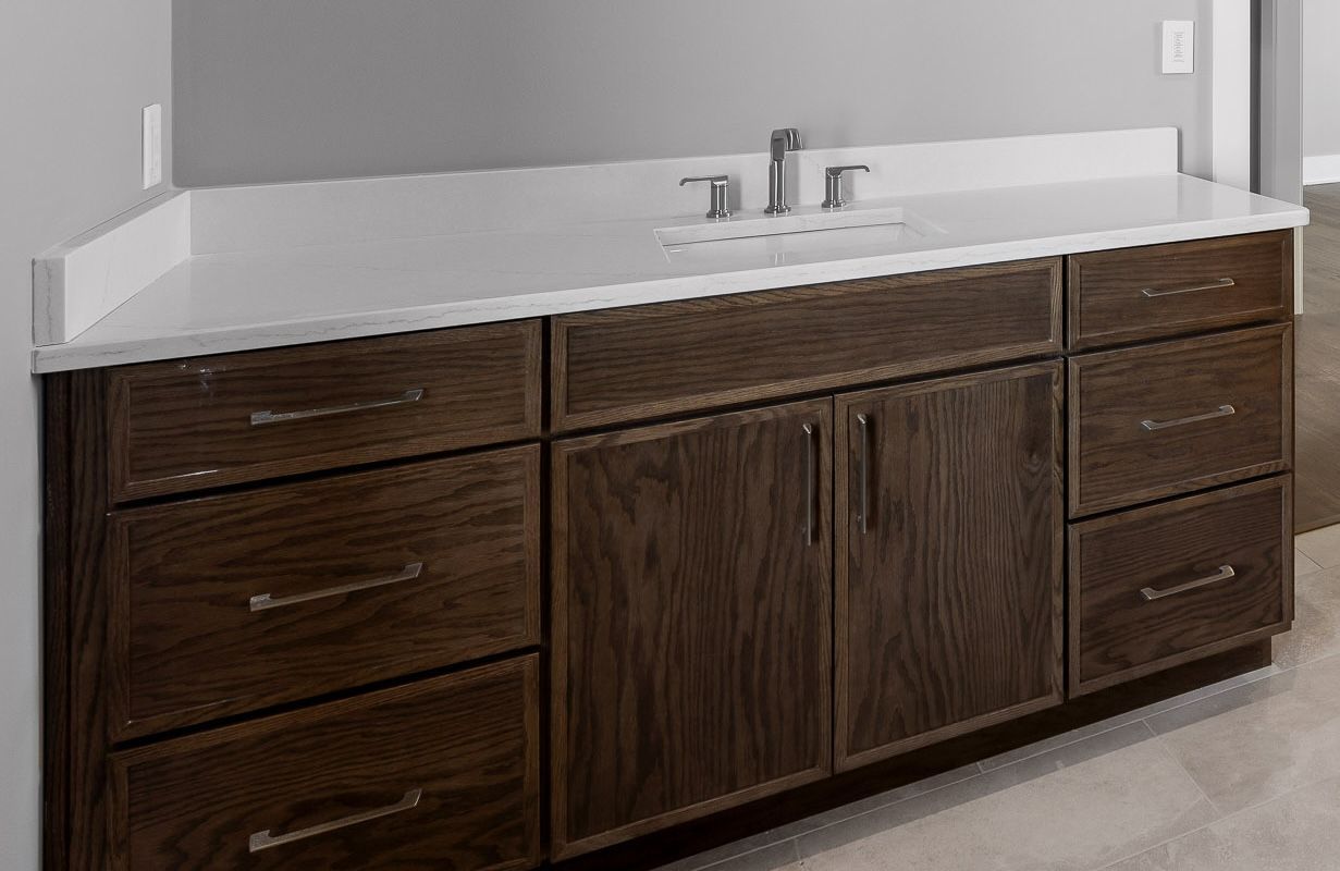 Dark wood bathroom vanity with a white countertop, drawers, and cabinet.