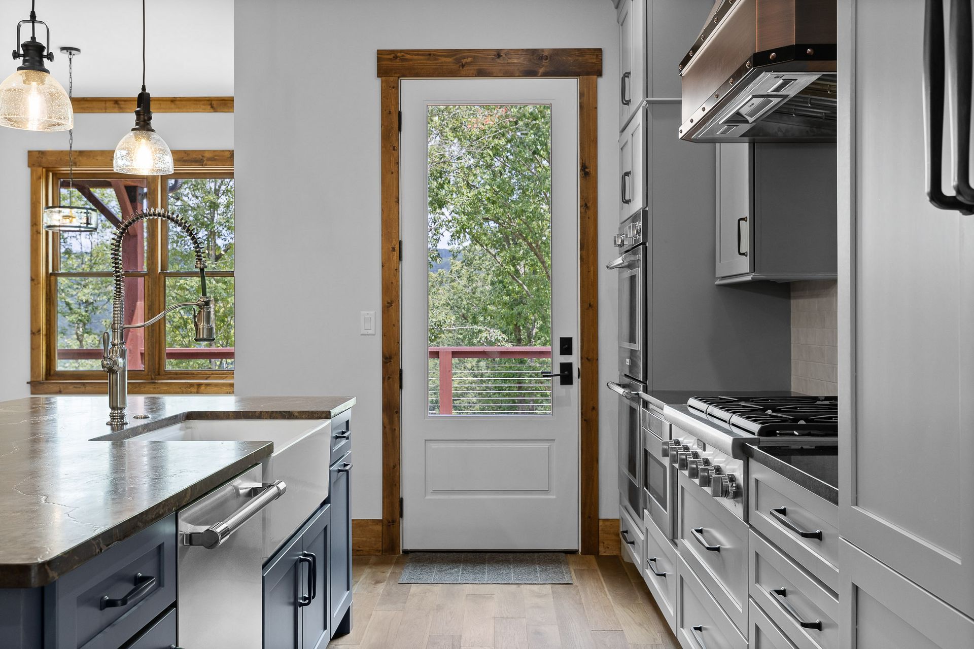 Kitchen with a white door to a balcony, gray cabinets, stainless appliances, and a farmhouse sink.