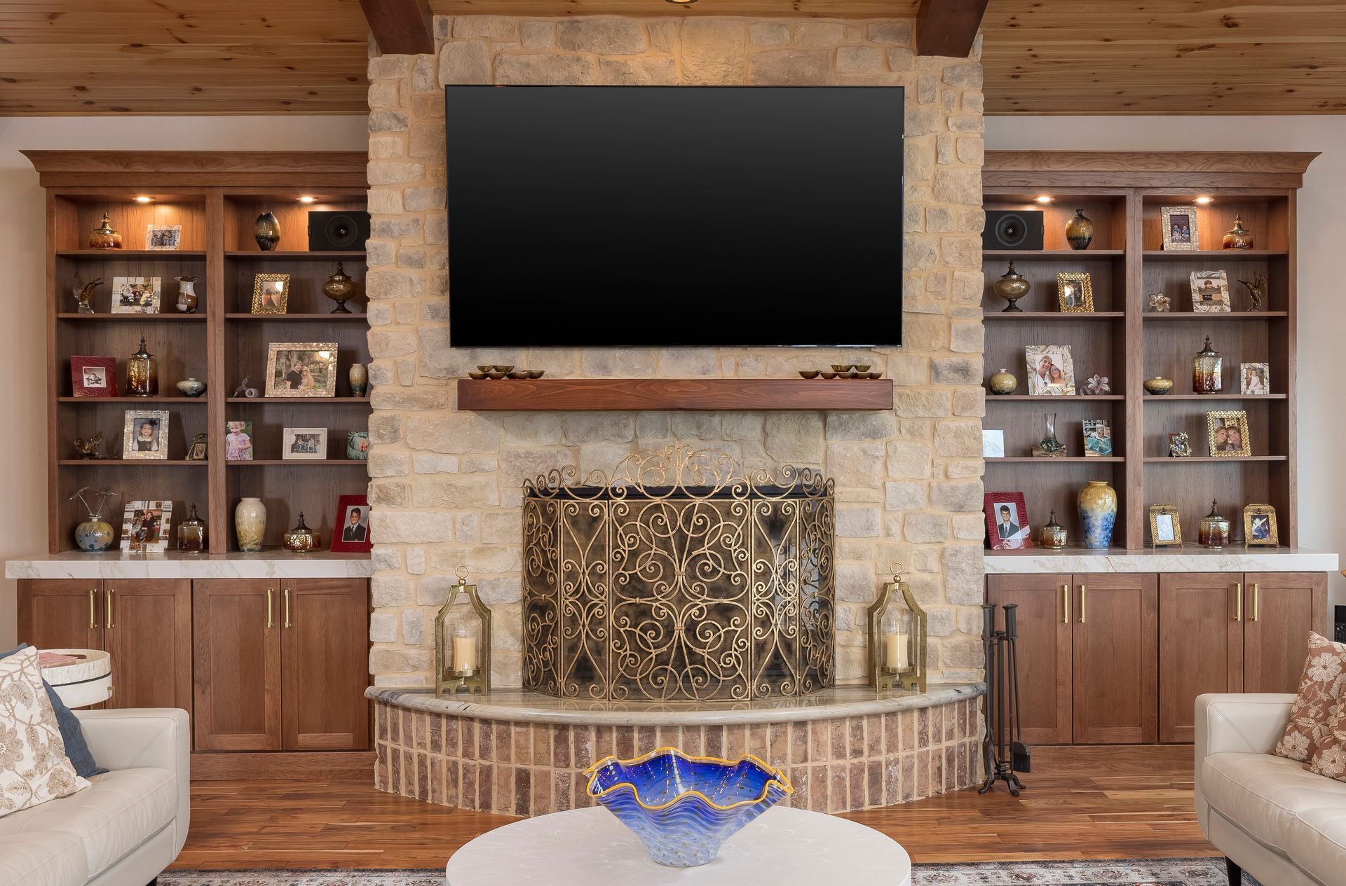Living room with fireplace, built-in bookshelves, large TV above, and two white couches.