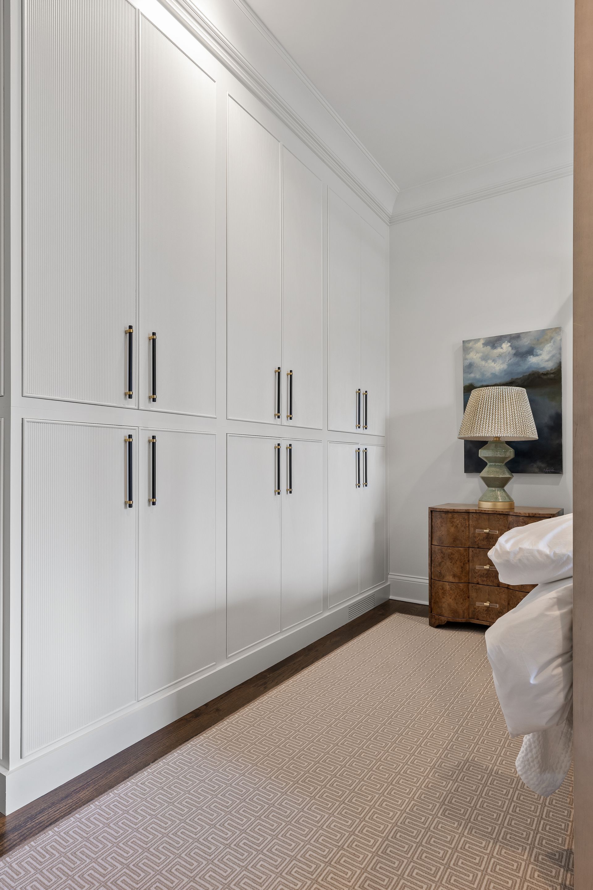 White built-in closets with silver handles in a bedroom with patterned carpet and a nightstand.