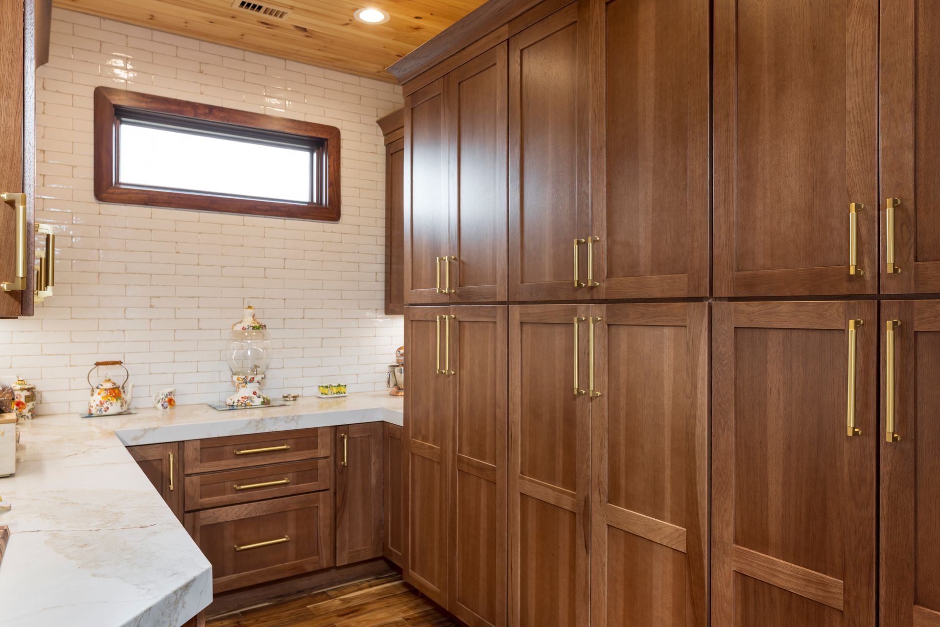 Kitchen with wooden cabinets, gold hardware, white countertops, and brick backsplash.