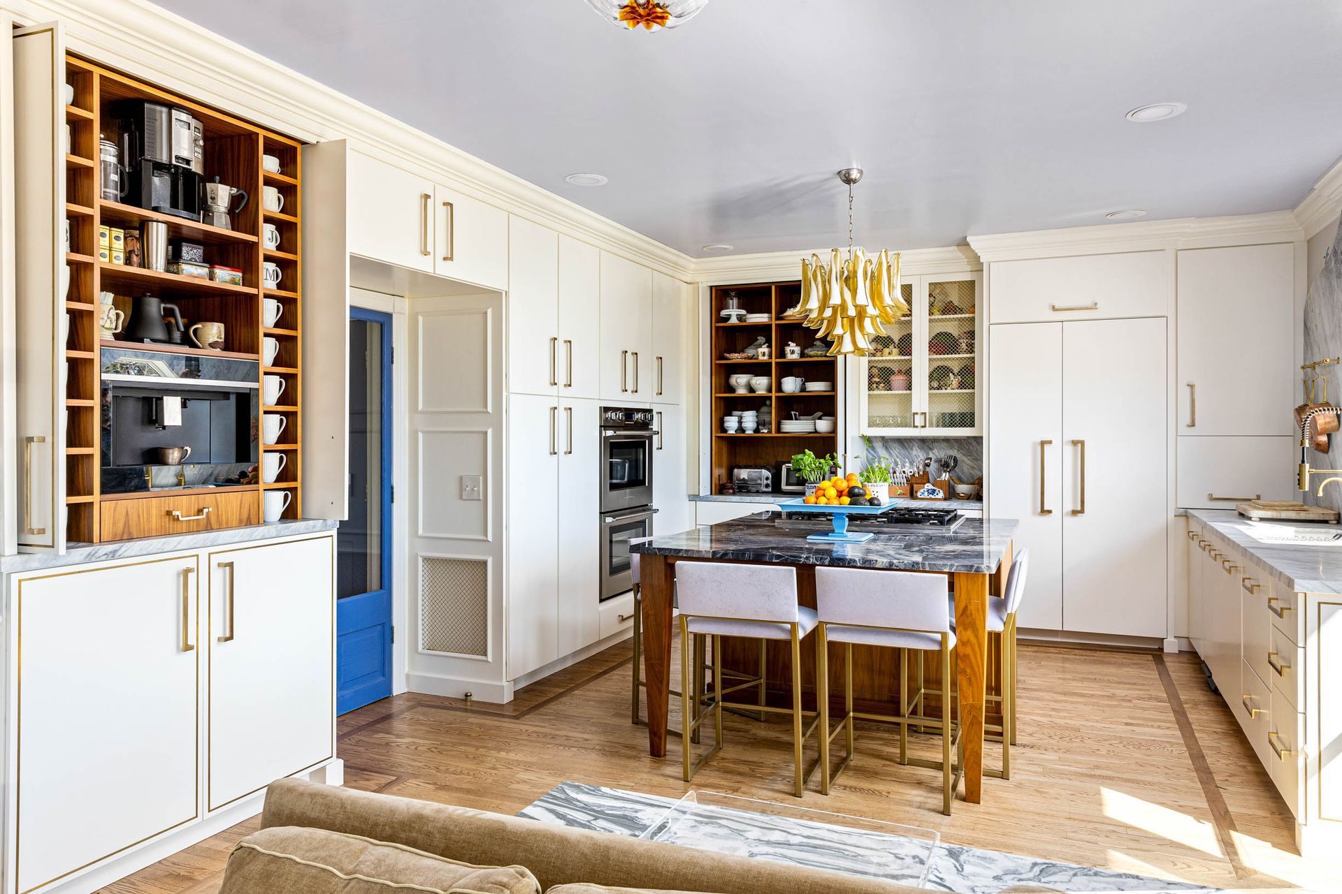 Elegant cream kitchen with island, gold accents, open shelving, and blue door.