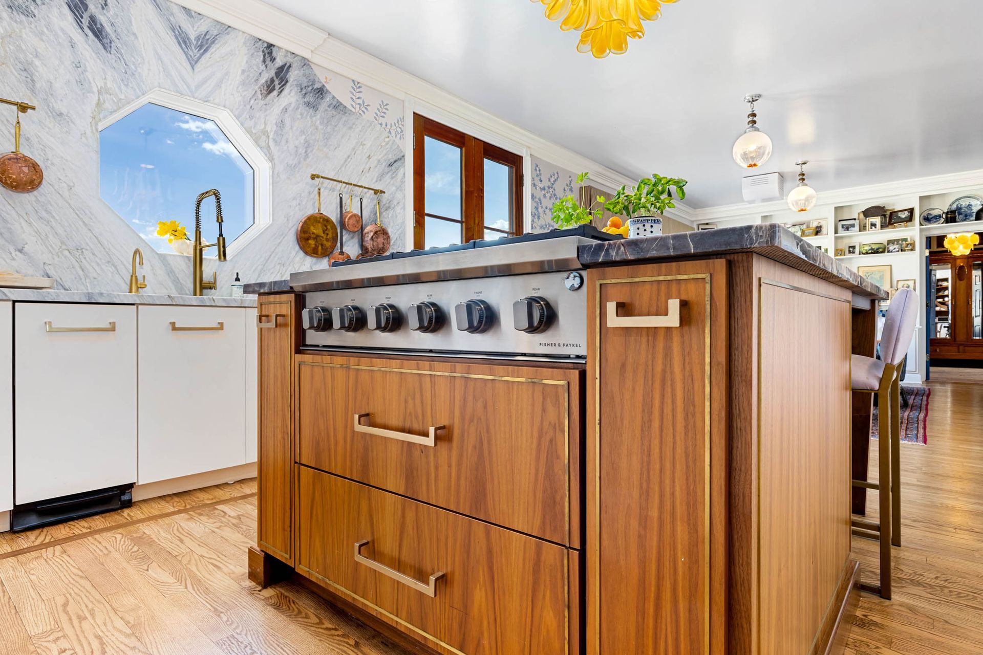 A luxurious kitchen featuring a wood island with a stove, marble backsplash, and gold accents.