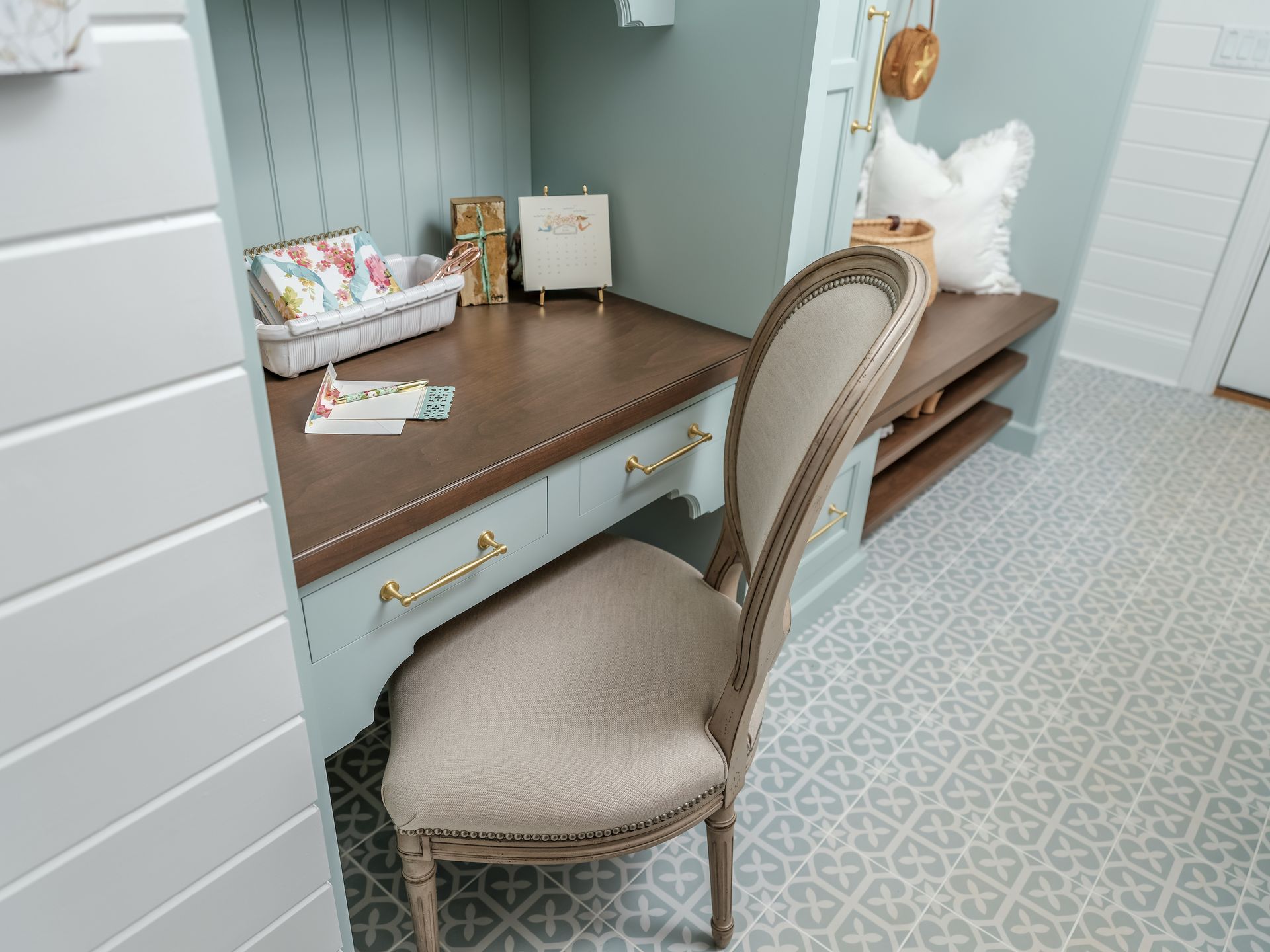 A cozy built-in desk nook painted blue-green with a wooden desk, a chair, and decorative items.