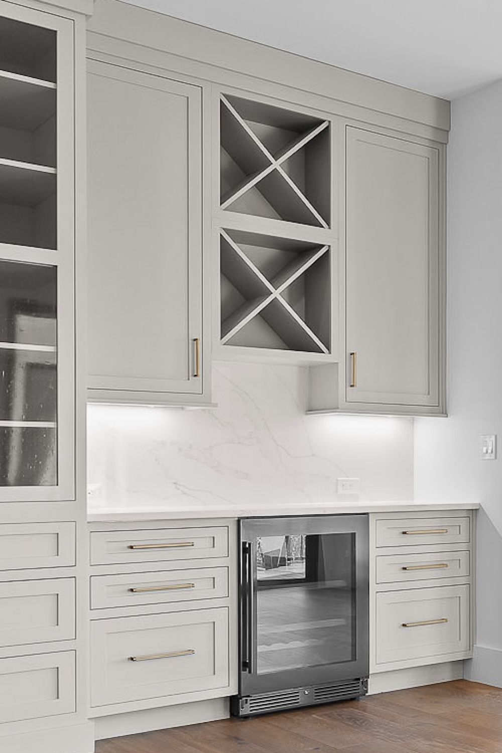 Gray built-in bar area with cabinets, wine rack, mini-fridge, and countertop.