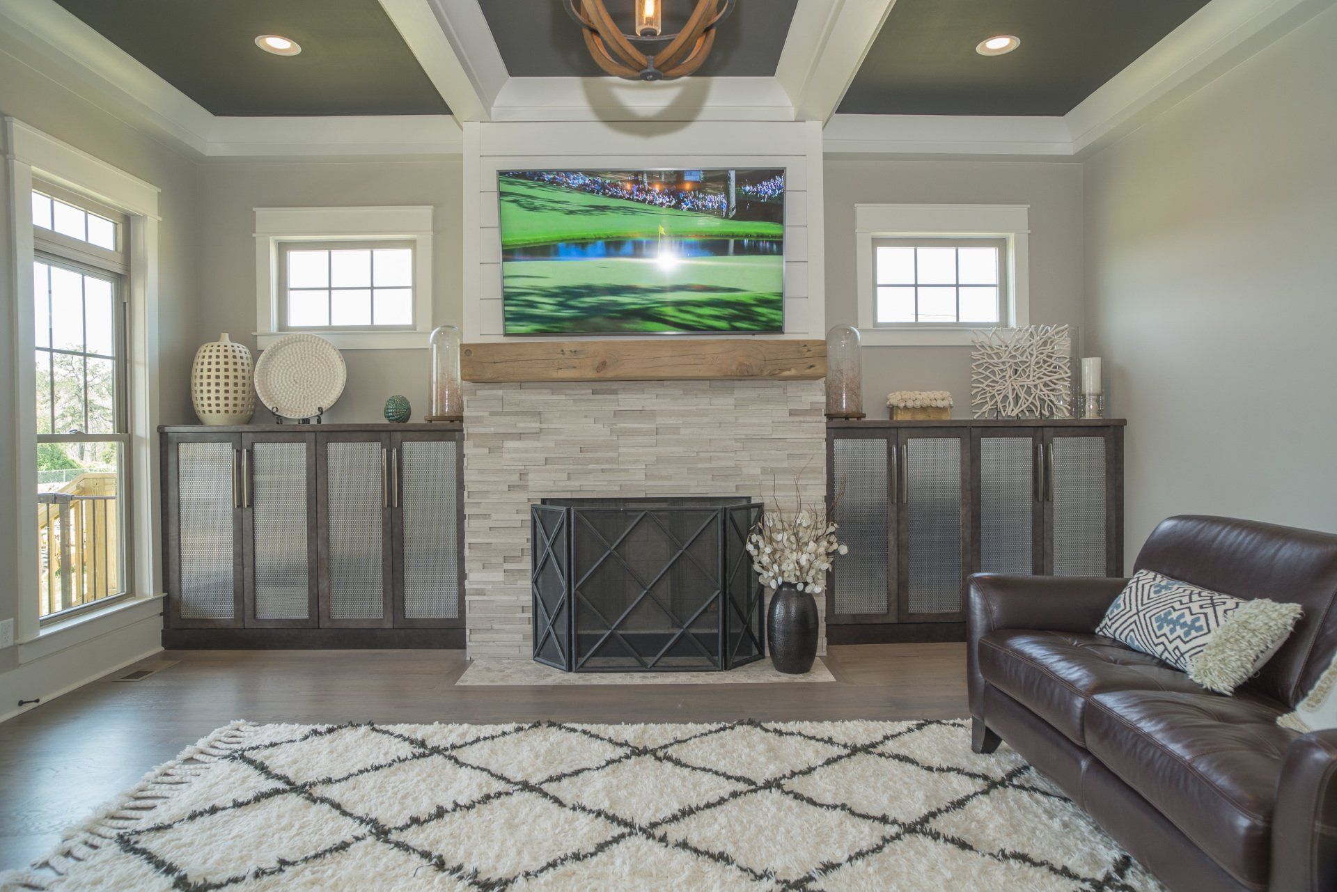 Living room with fireplace, TV, and brown leather sofa. Gray walls, white rug, and dark wood cabinets.