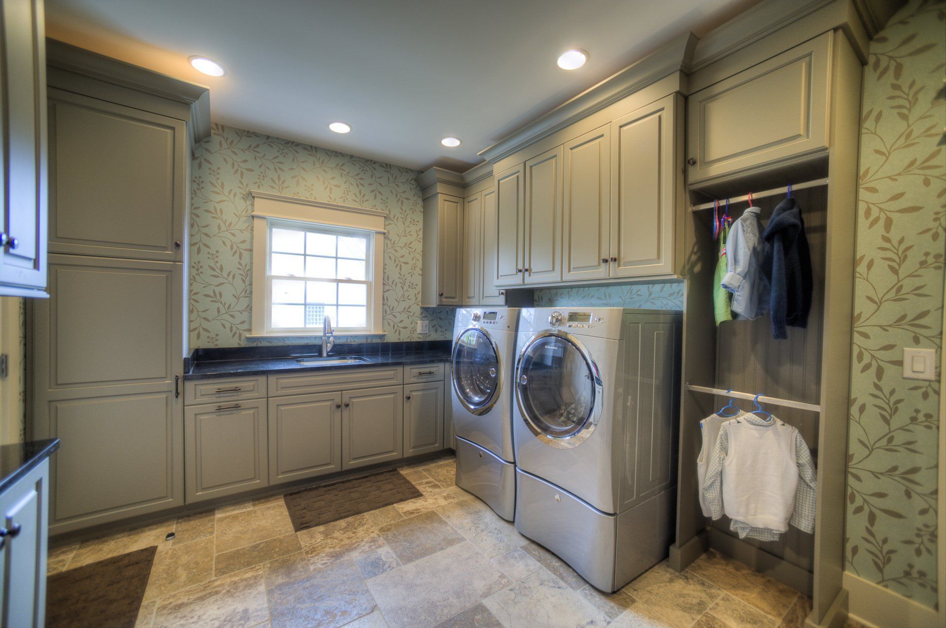 Laundry room with gray cabinets, washer/dryer, window, and clothes hanging in a closet.