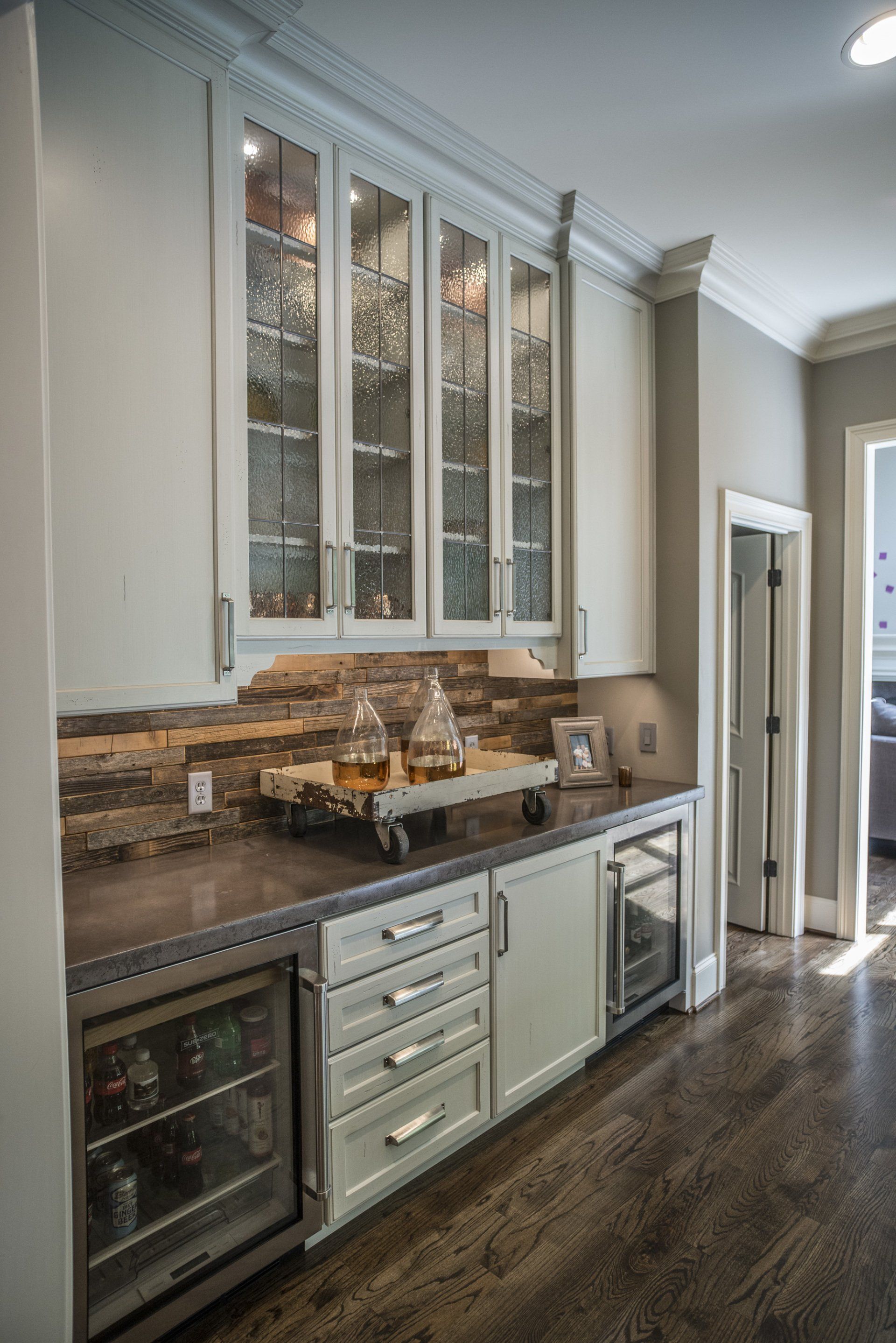 Built-in home bar with glass-front cabinets, a stone backsplash, and a dark countertop.