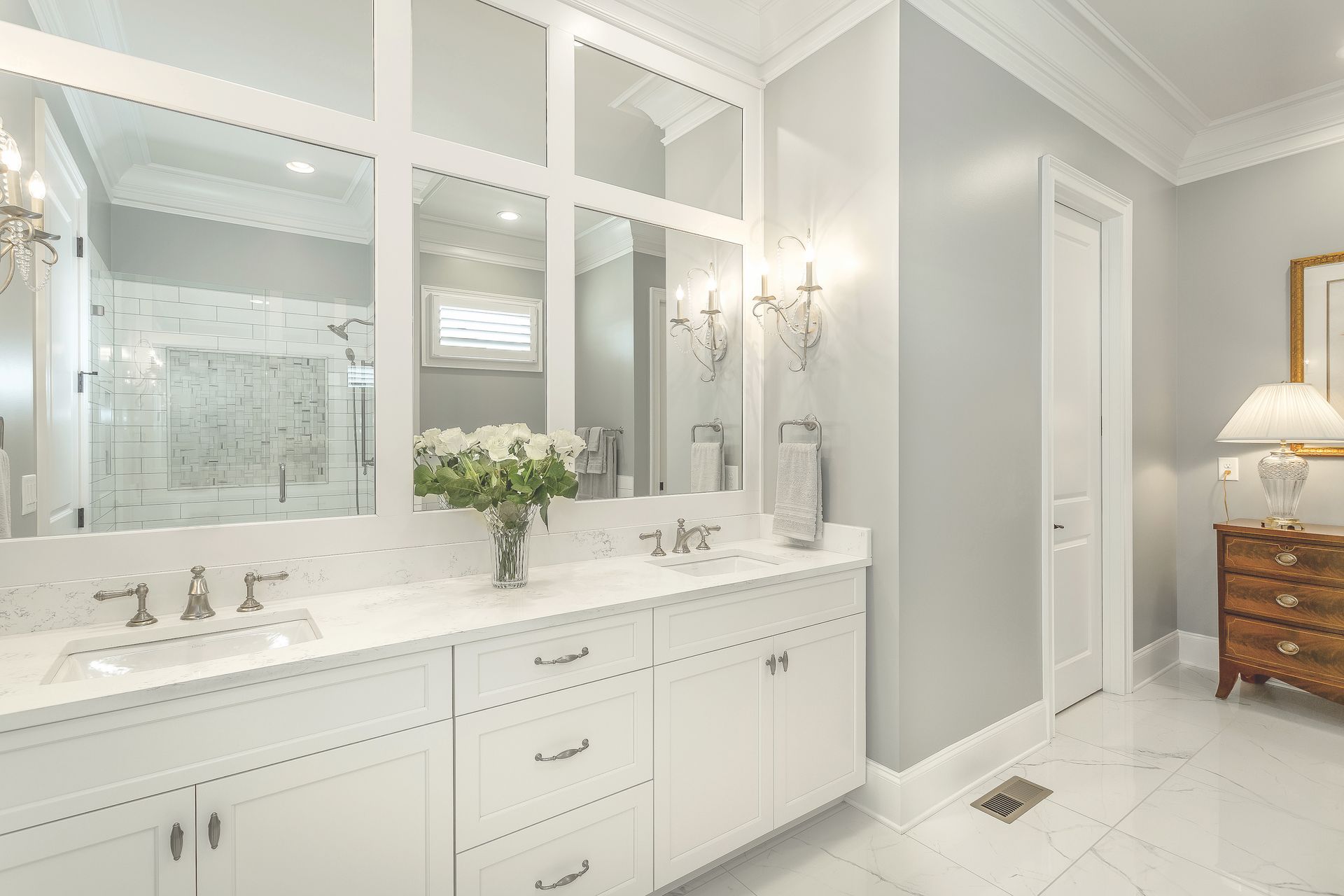 Bathroom with white cabinets, gray walls, large mirror, and floral arrangement.