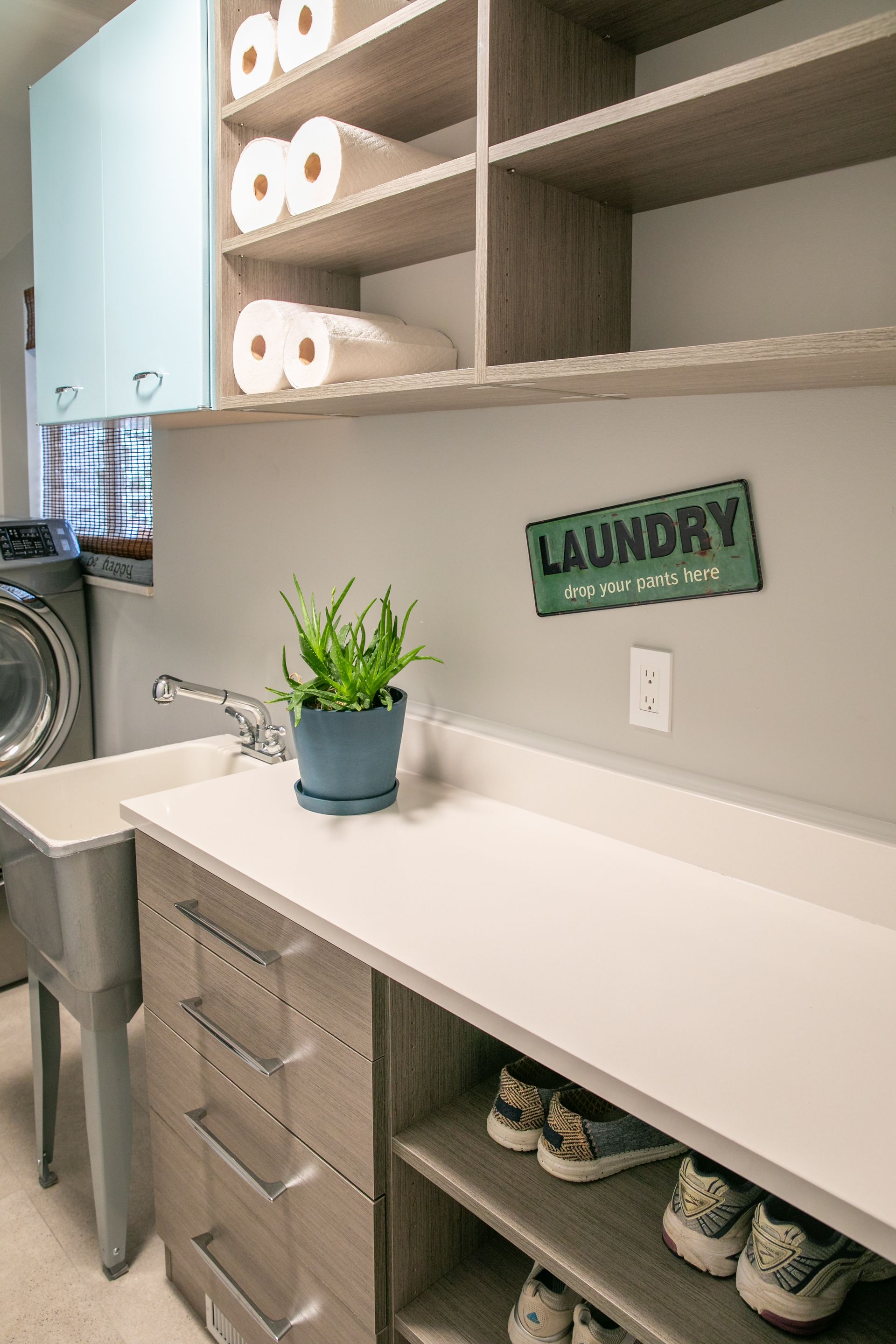 Laundry room with white countertop, wooden cabinets, and a sink; a blue cabinet is above.