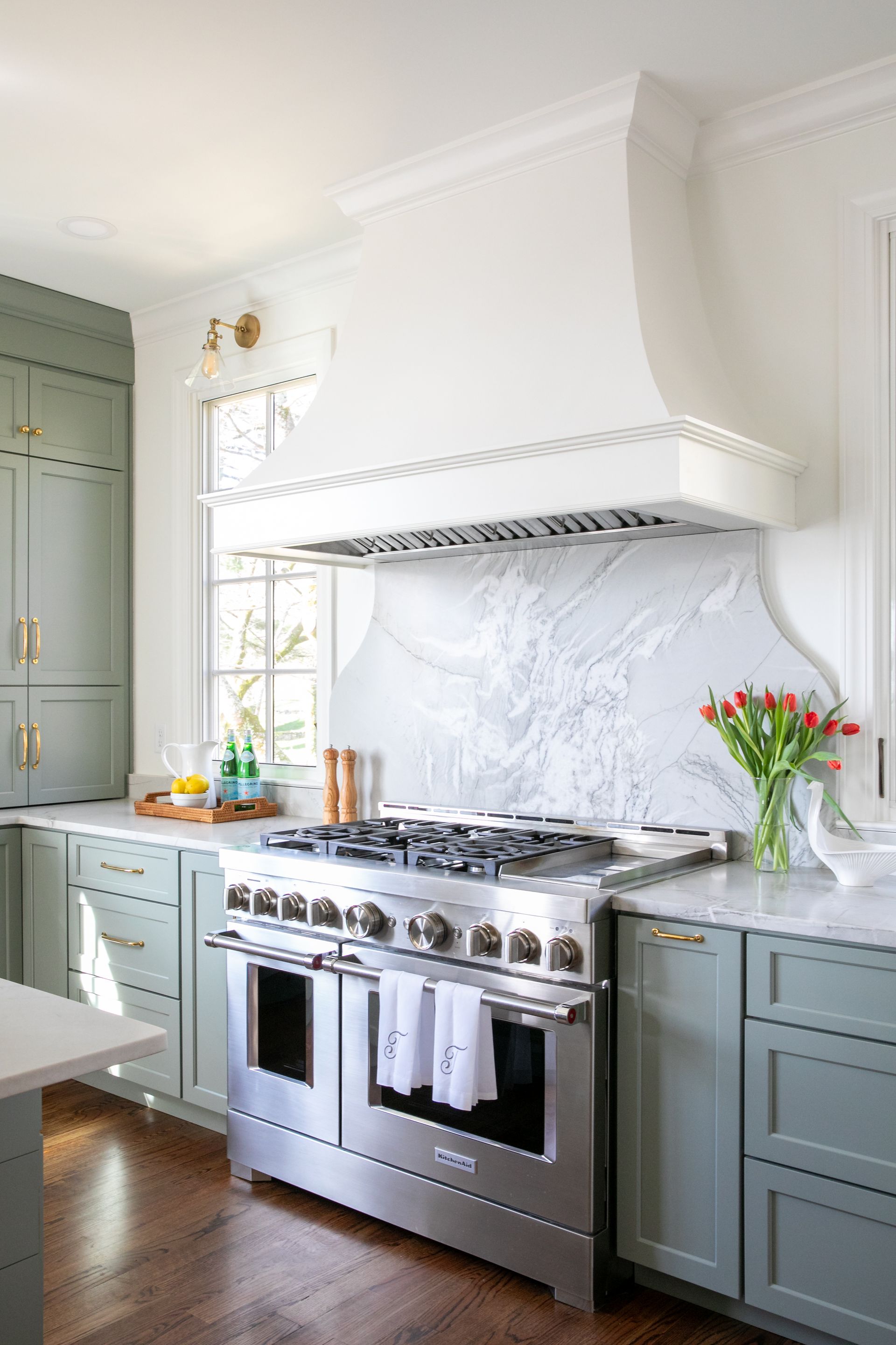 Green kitchen with stainless steel range, white marble backsplash, and range hood.