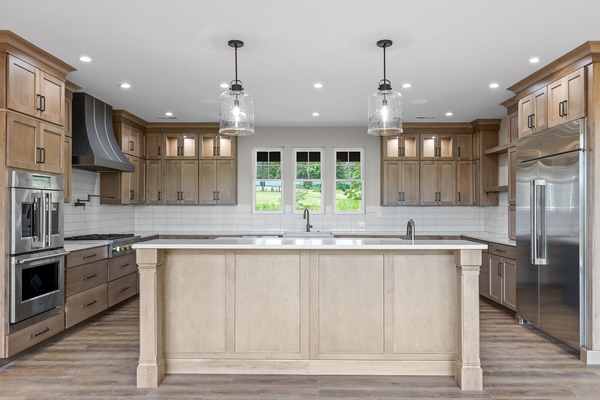 A modern kitchen with light wood cabinets, stainless steel appliances, and a large island.