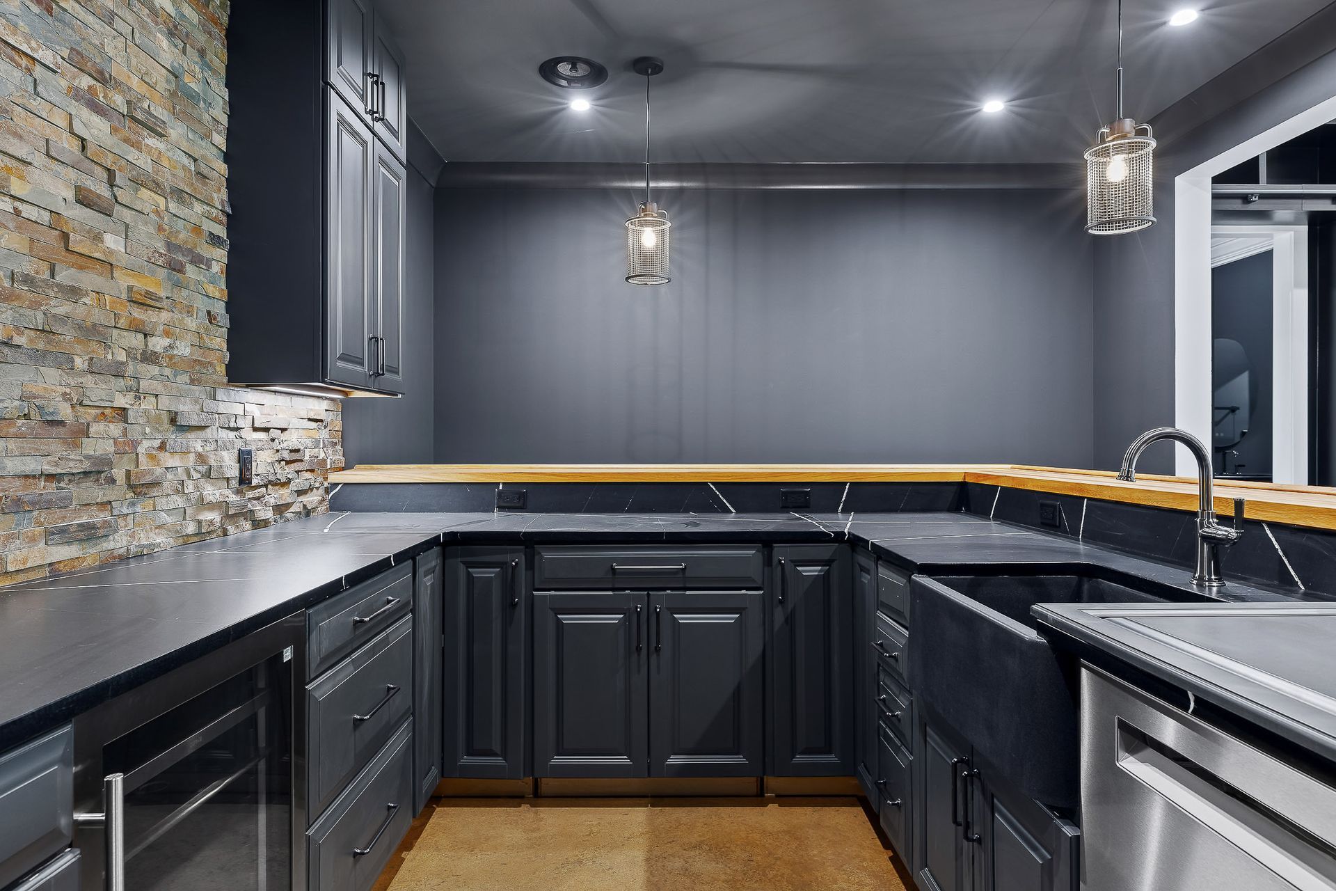 Dark gray kitchen with stone accent wall, wood countertop, and stainless steel sink.