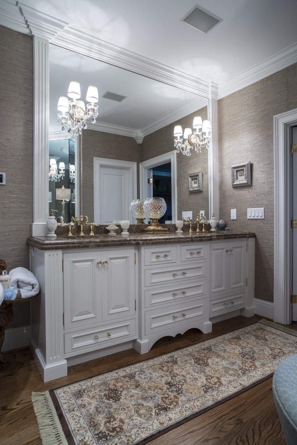 Bathroom with white vanity, large mirror, two sinks, chandeliers, and patterned rug.
