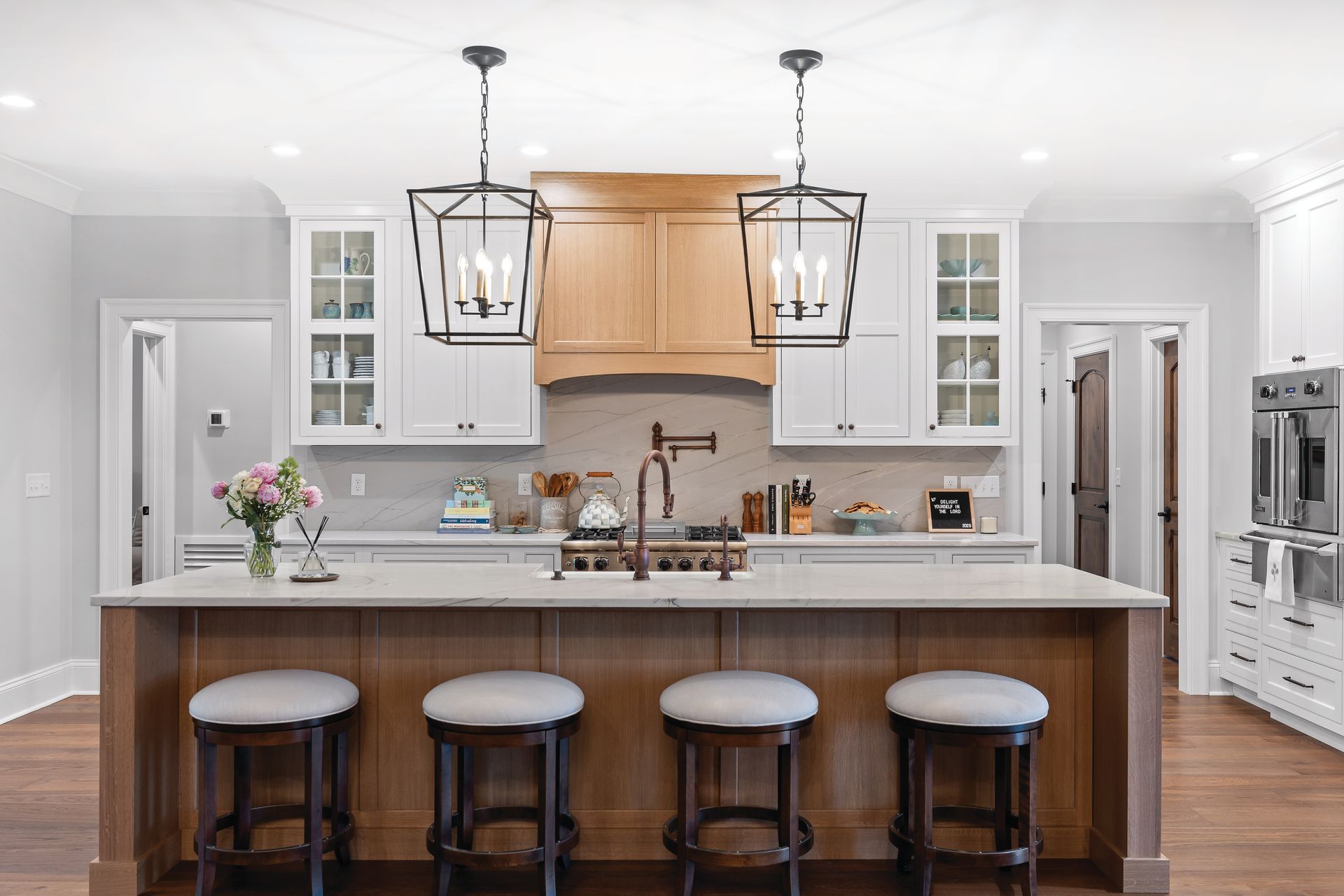 Modern kitchen with island, four bar stools, pendant lights, light wood cabinets, and white countertops.
