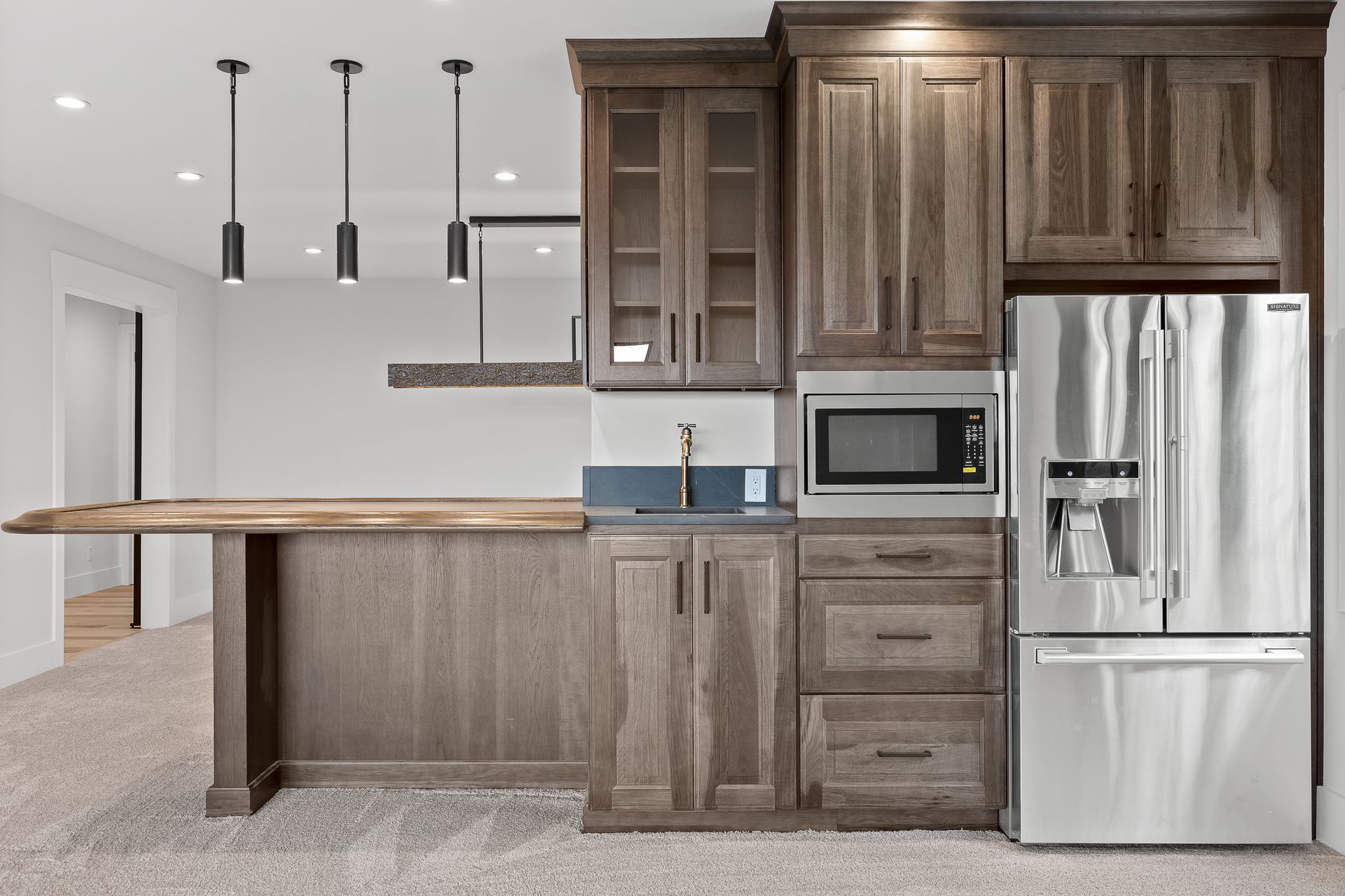 Basement bar area with wood cabinets, a sink, microwave, and refrigerator.  A wooden bar top extends to the left.