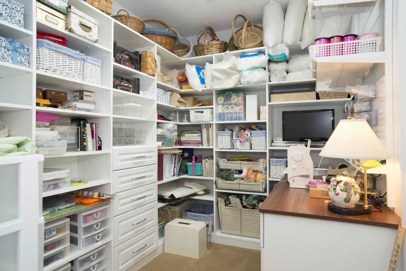 White-shelved craft room filled with supplies, including baskets, boxes, and a small TV.