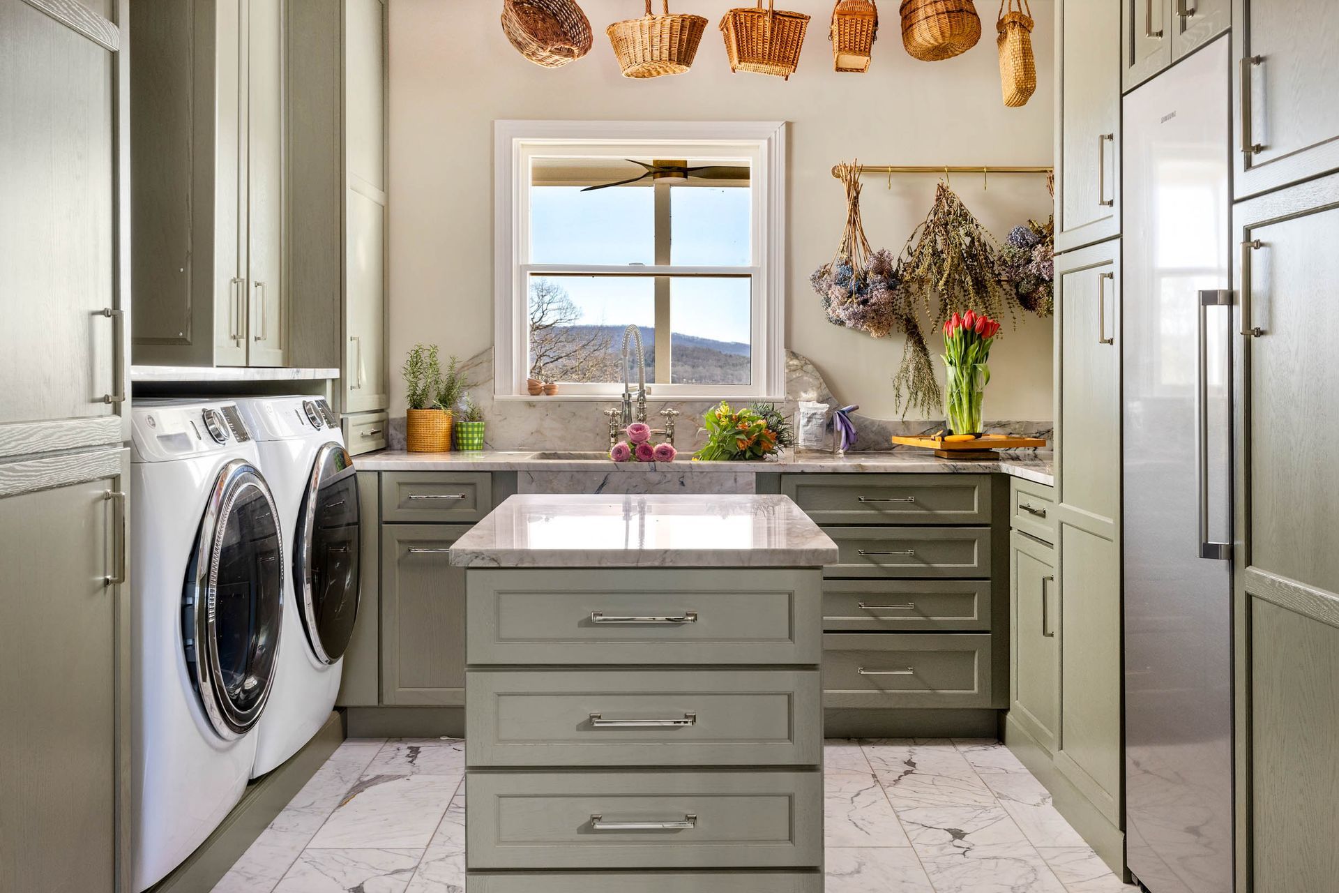 Laundry room with sage green cabinets, stainless steel appliances, and a marble-look tile floor.