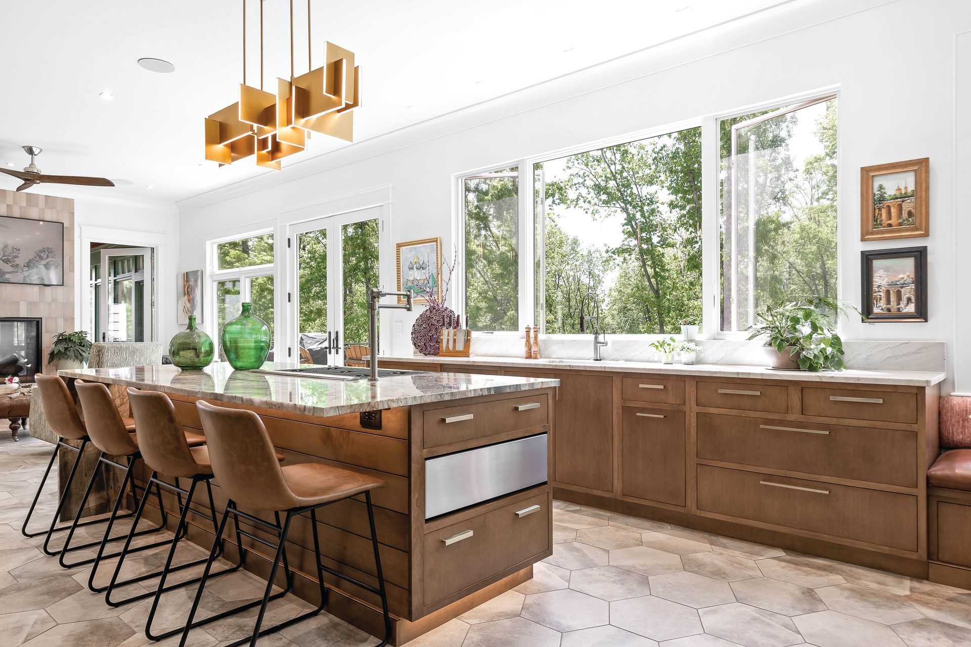 Spacious kitchen with a large island, bar seating, and expansive windows overlooking trees.