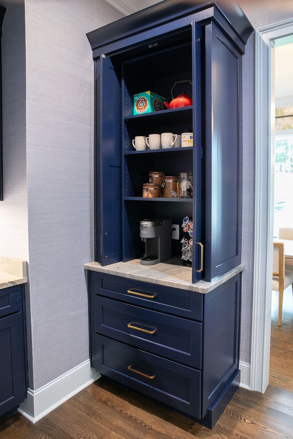 Navy blue built-in coffee station: cabinet with open doors, drawers below, mugs and coffee maker inside.