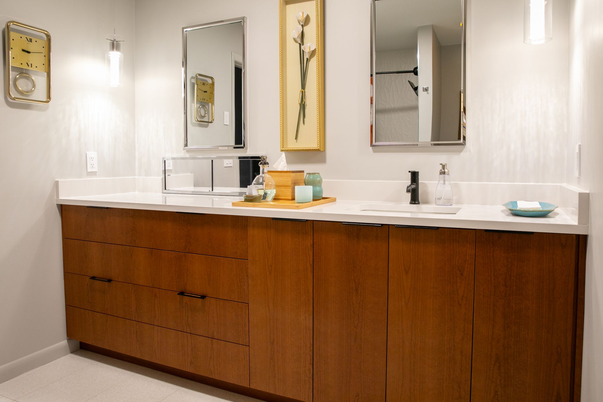 Bathroom with a long wooden vanity, mirrors, and artwork. White countertop and light walls.