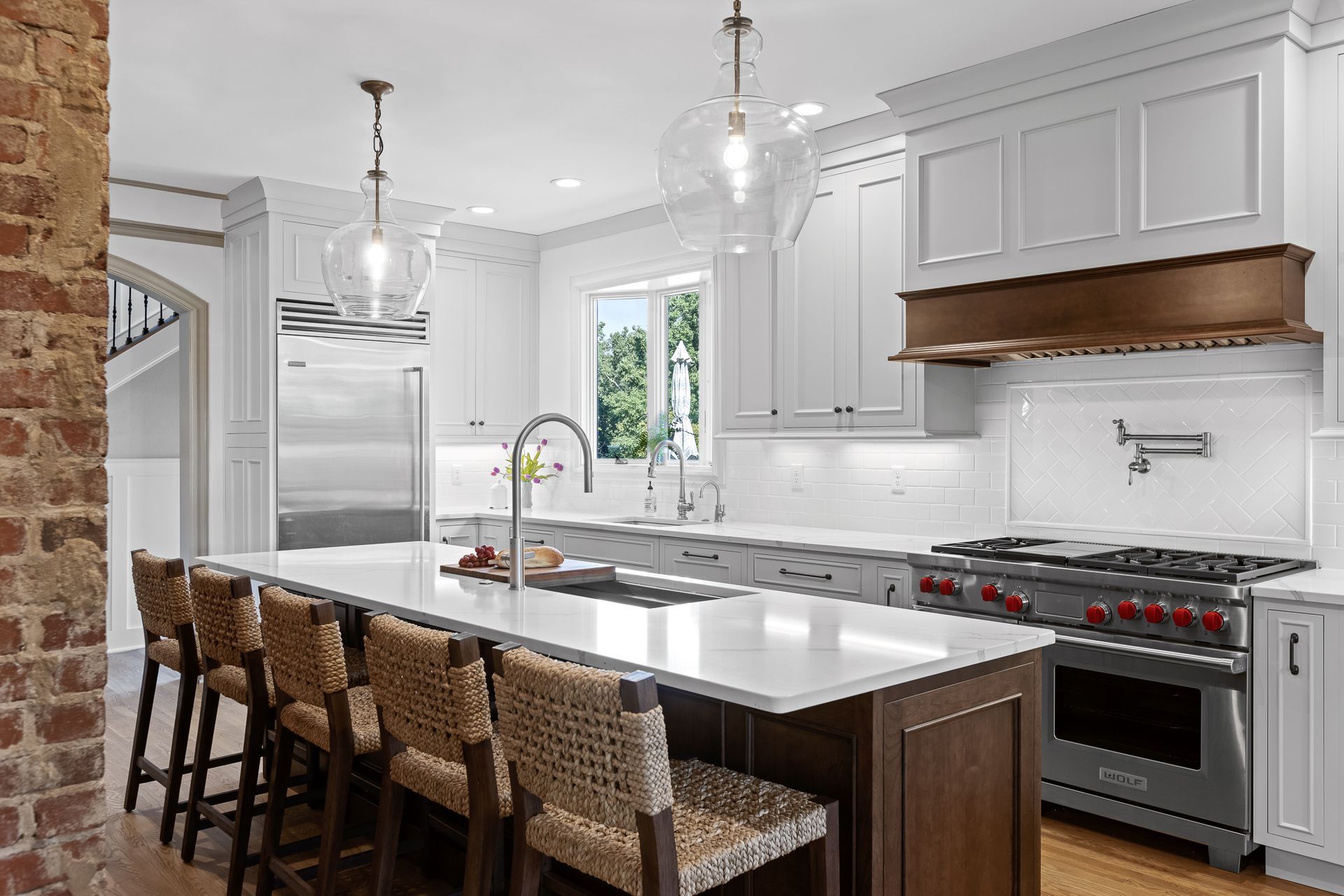 Elegant kitchen with a large island, white cabinets, and a red brick wall.