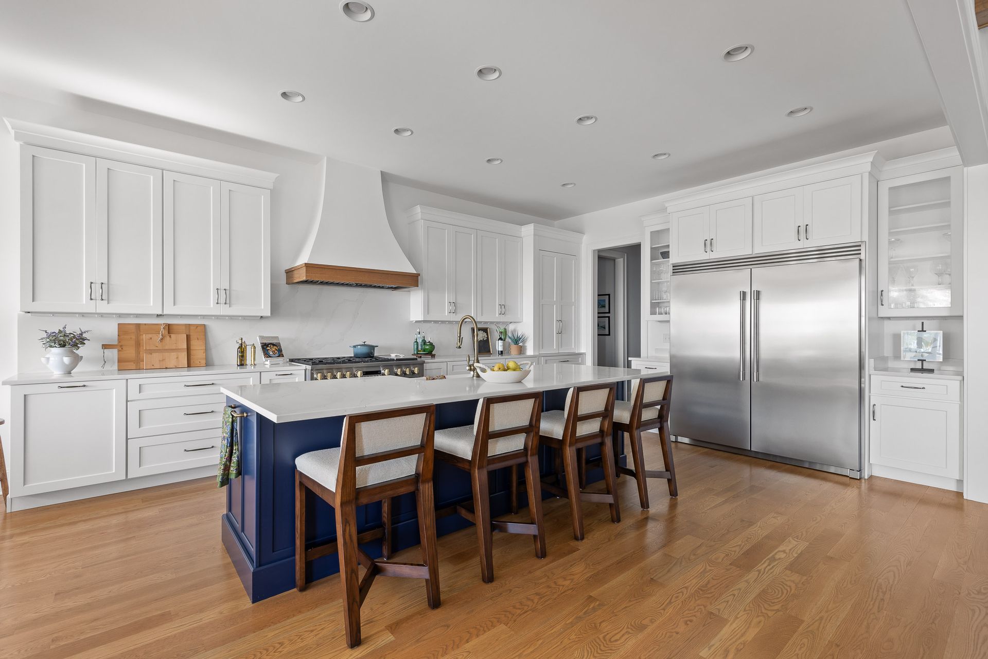 White kitchen with blue island and wooden bar stools.