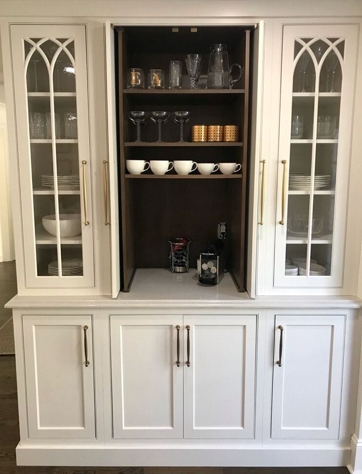White built-in cabinet with glass-fronted doors, a central lift-up bar section, and lower storage.