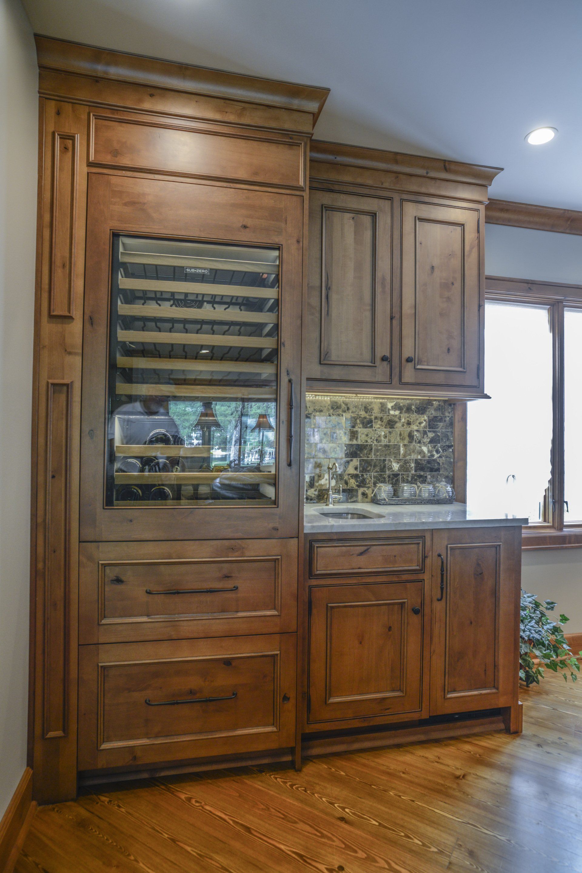 Wooden built-in bar with a wine fridge, cabinets, drawers, and a countertop in a home's interior with a wood floor.