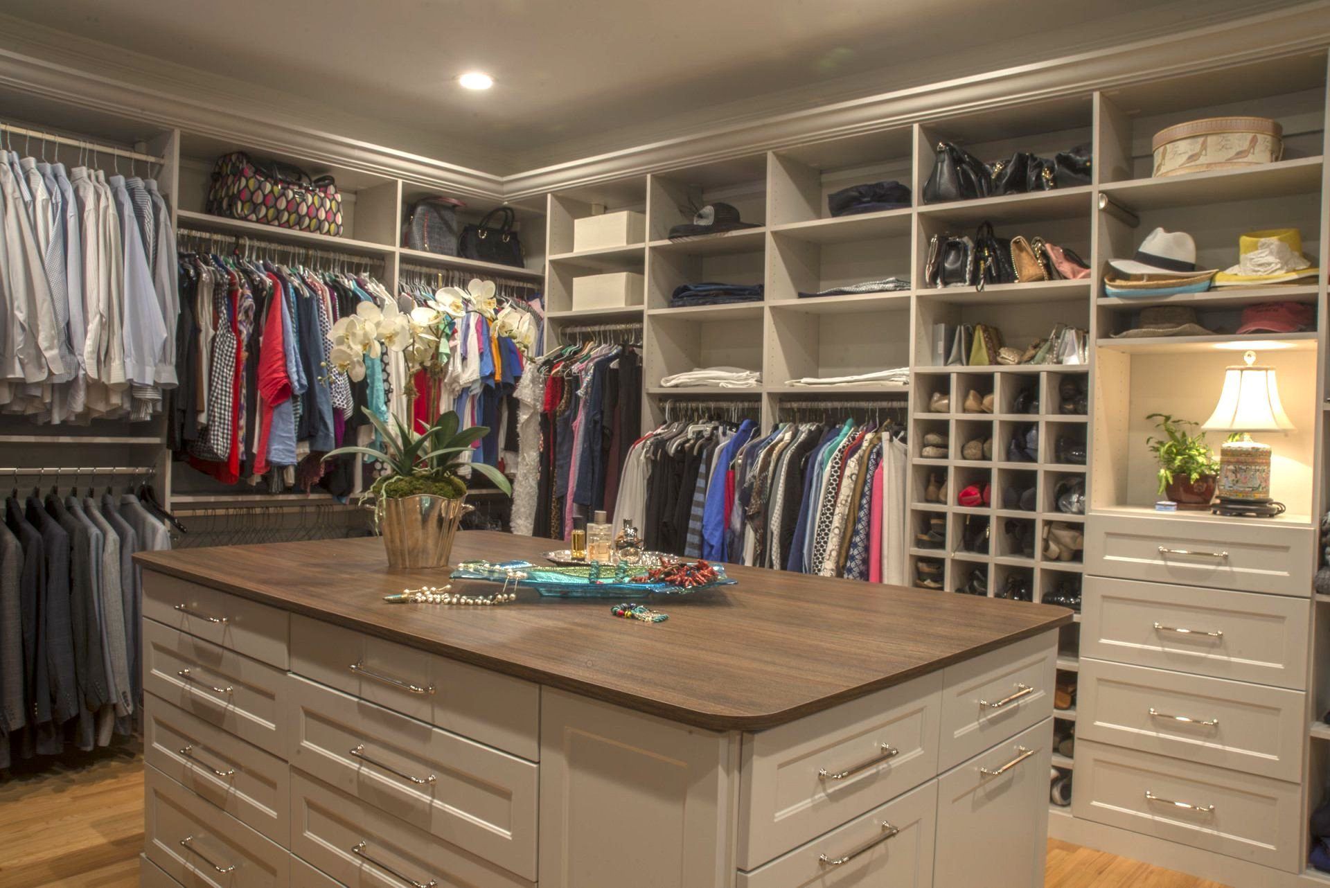 Walk-in closet with custom white cabinetry, central island, and clothes neatly organized.