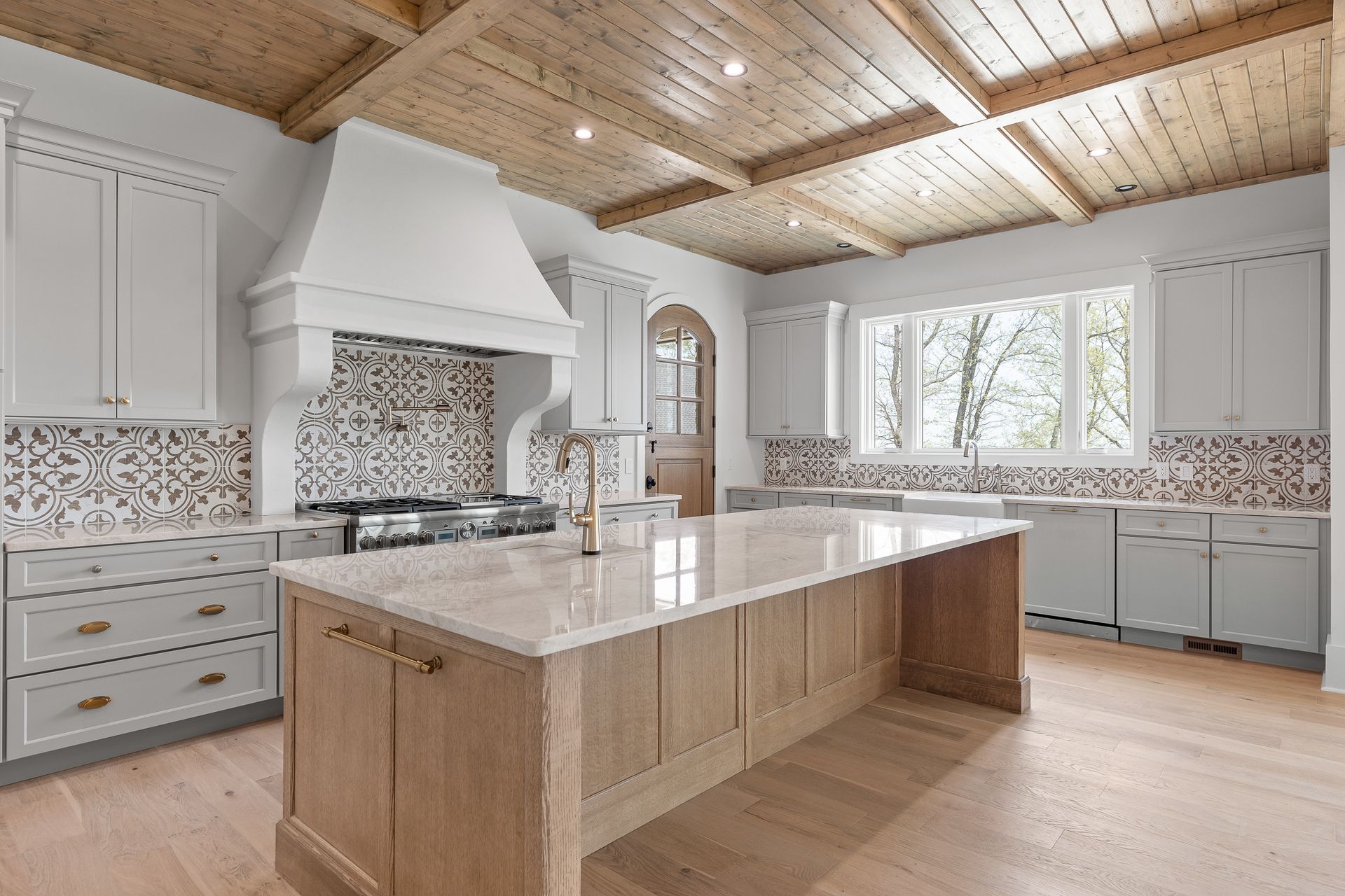 Kitchen with light wood ceiling and island, light gray cabinets, and patterned backsplash.