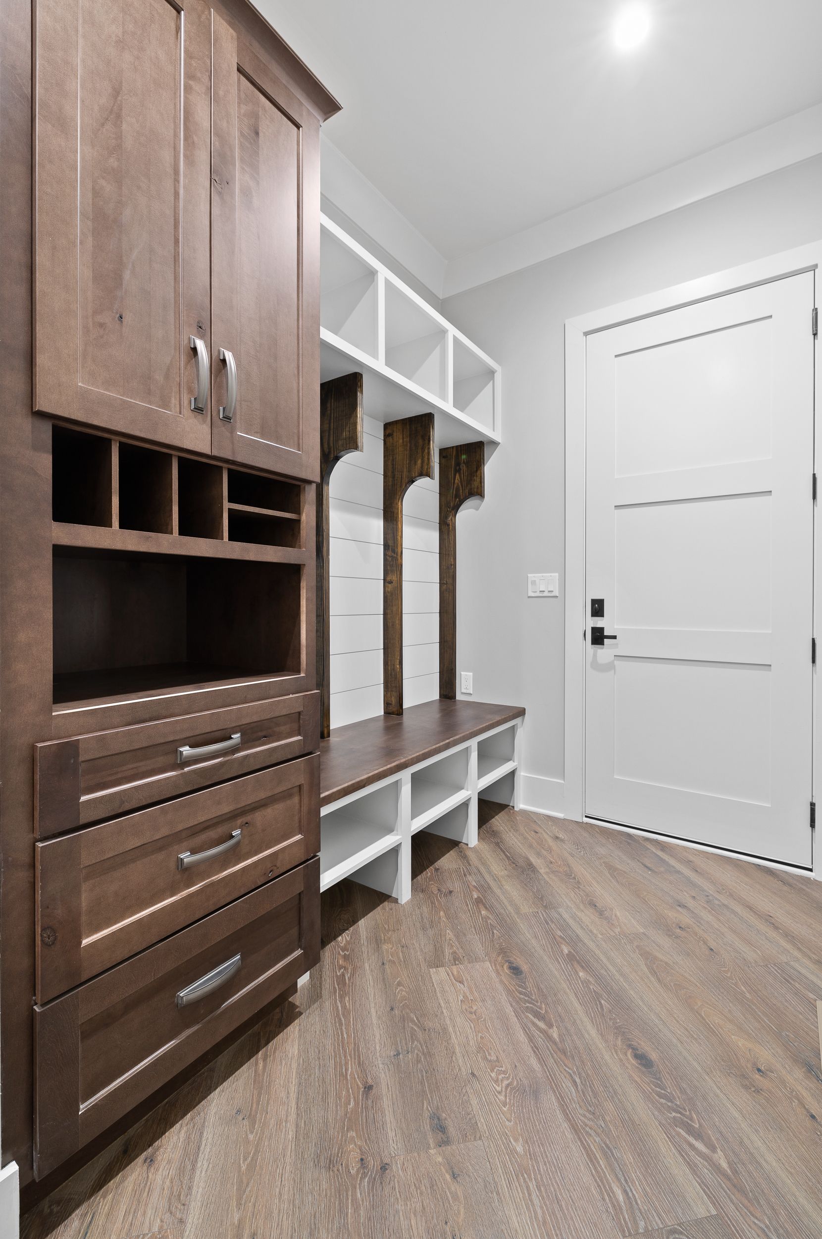 Mudroom with wood and white storage, bench, drawers, and a white door.
