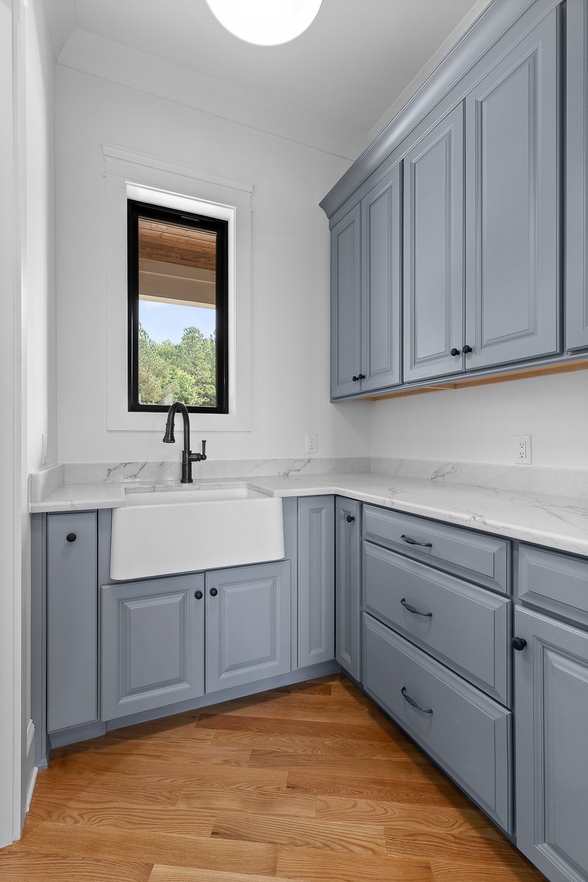 Laundry room with blue cabinets, white sink, and wood floor.