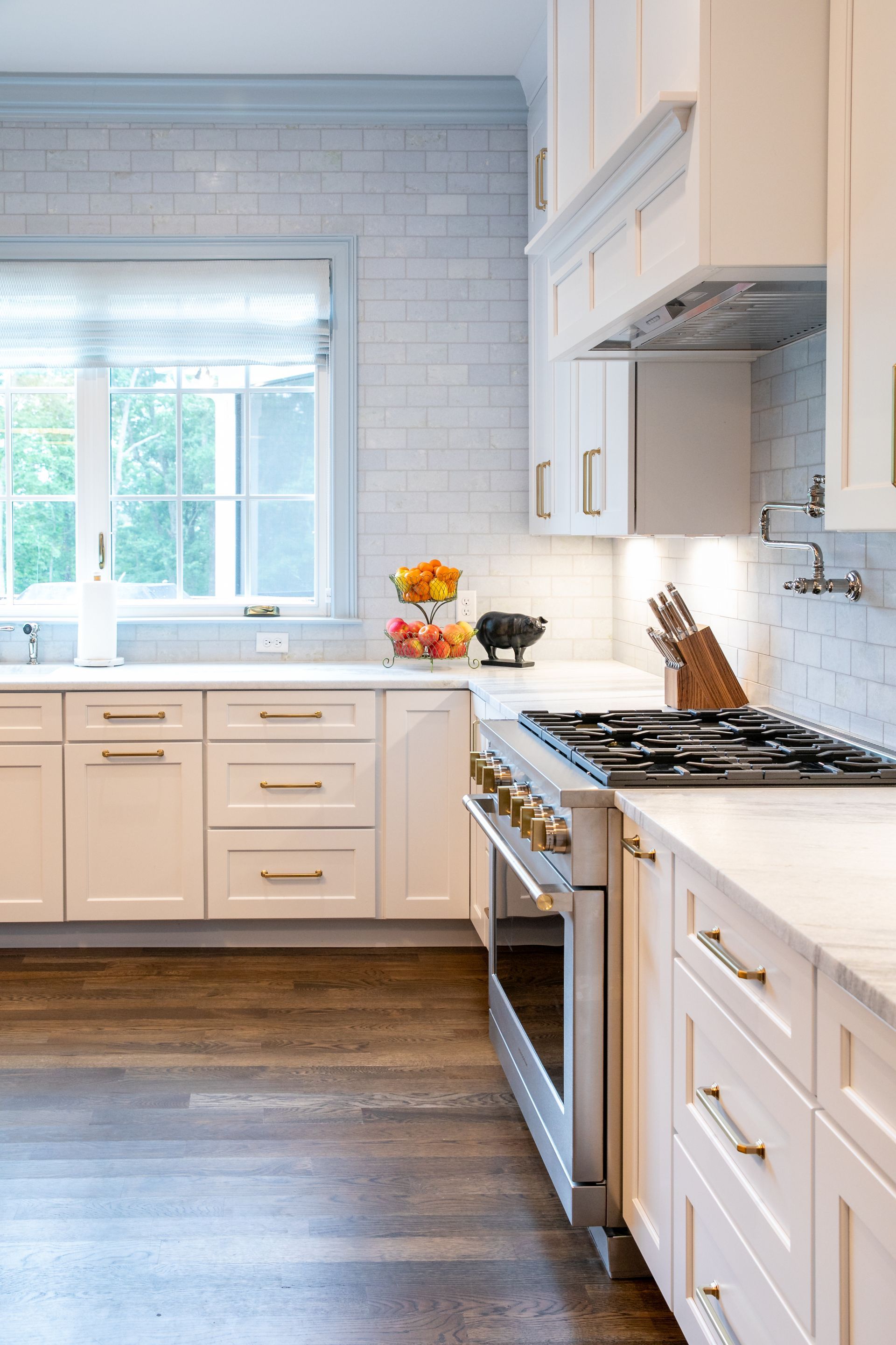 White kitchen with light wood floors, stainless steel range, and gold hardware.