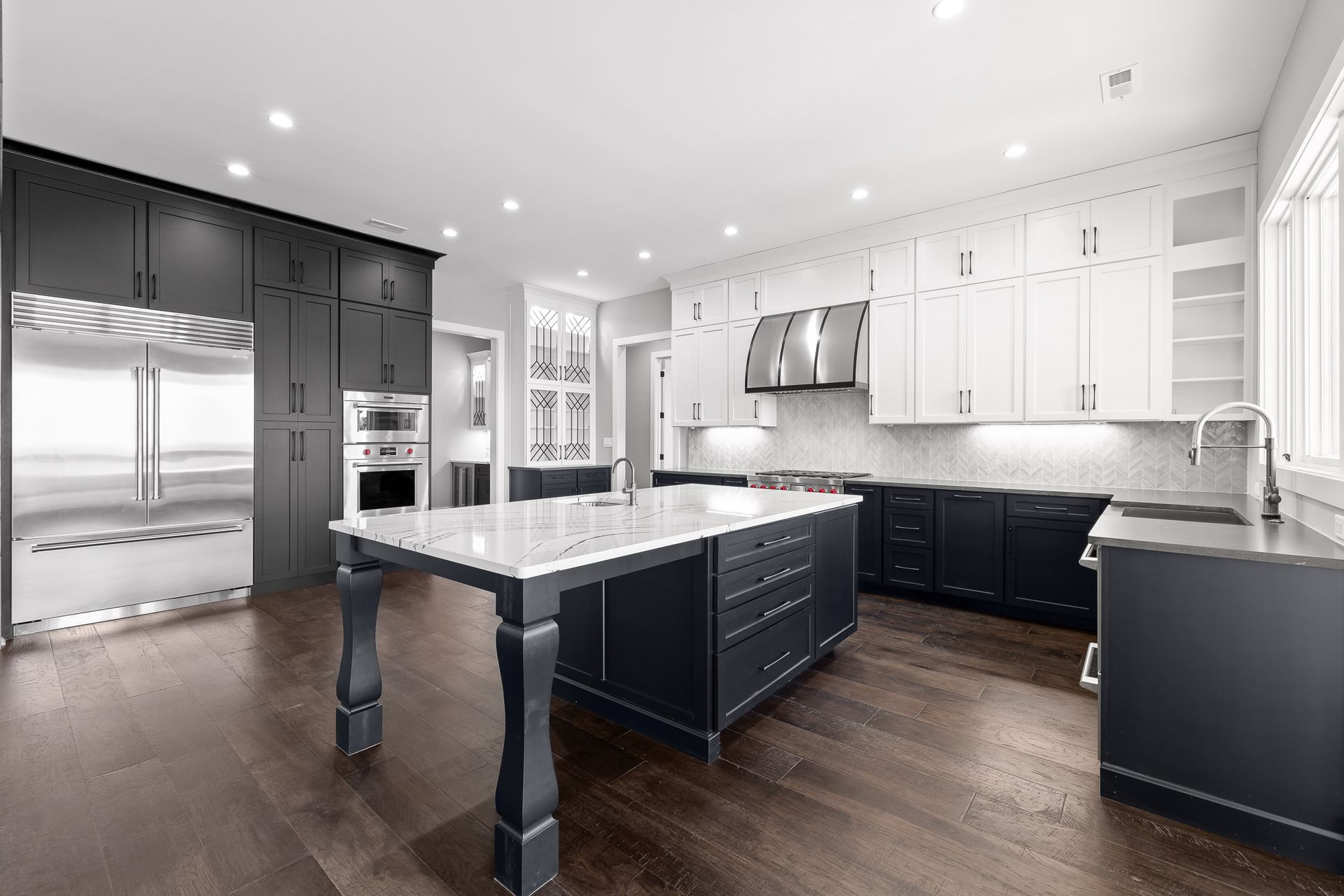 Modern kitchen with dark blue and white cabinets, stainless steel appliances, and a marble island.