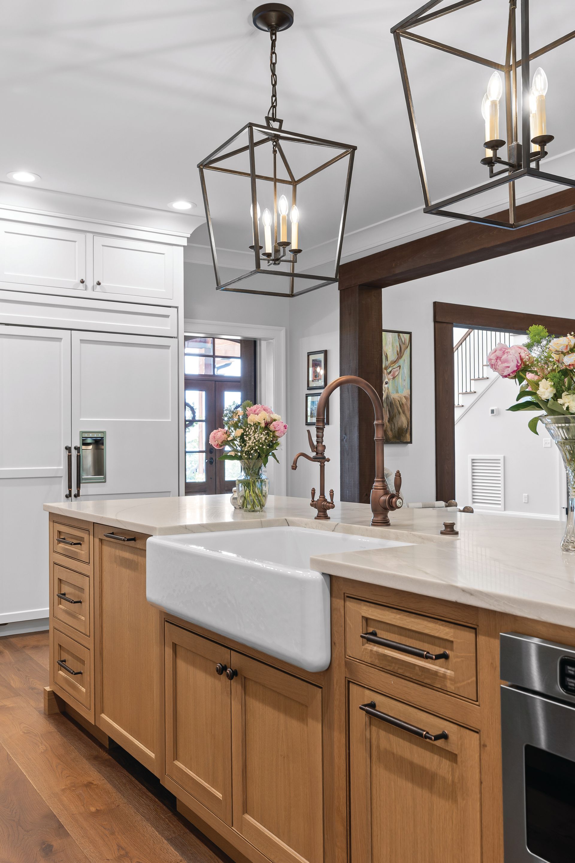 Kitchen with light wood cabinets, white apron sink, and dark pendant lights.