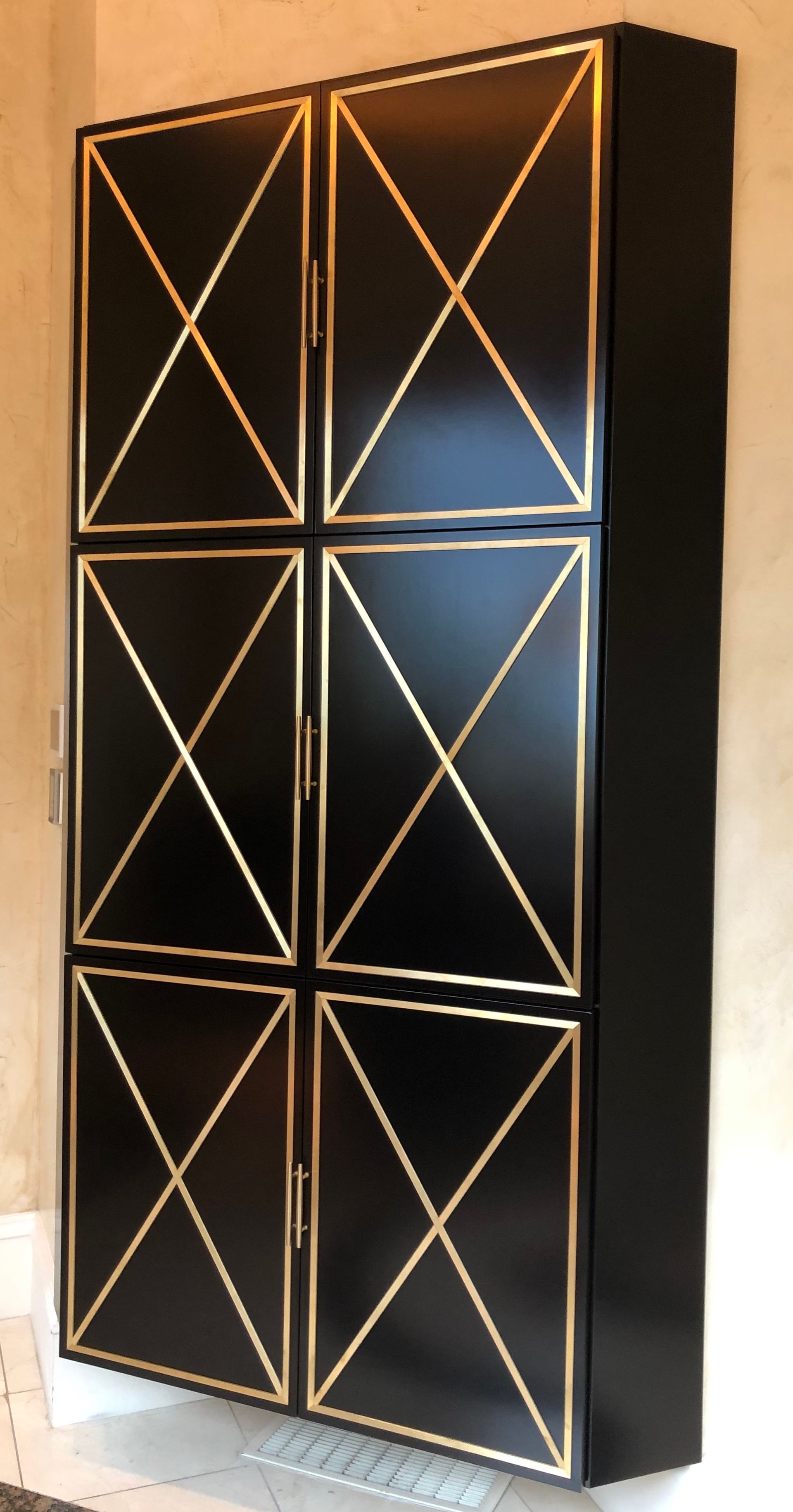 Black cabinet with gold geometric accents on a tan wall.