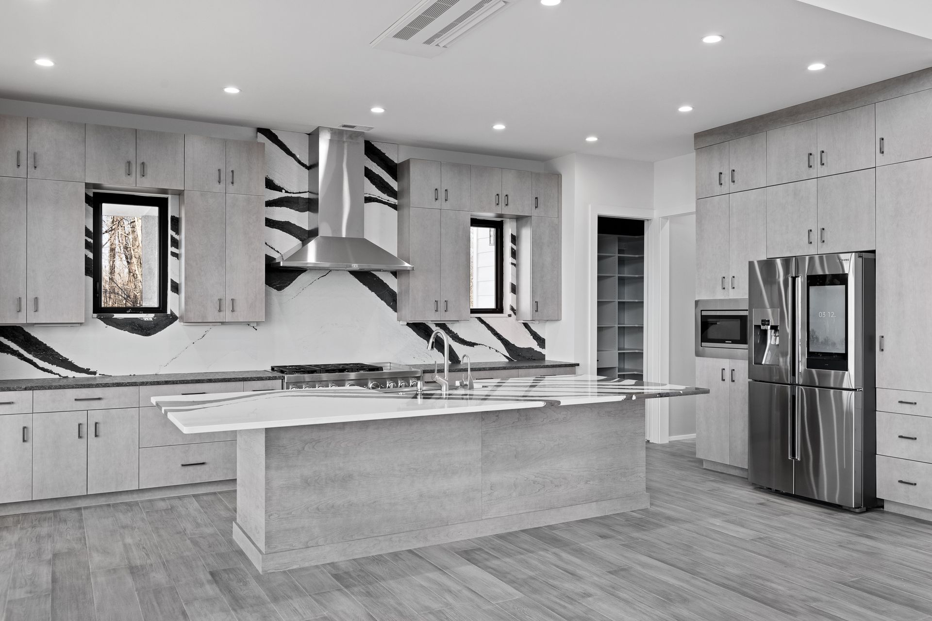 Modern kitchen with gray cabinets, island, stainless steel appliances, and black accent wall.