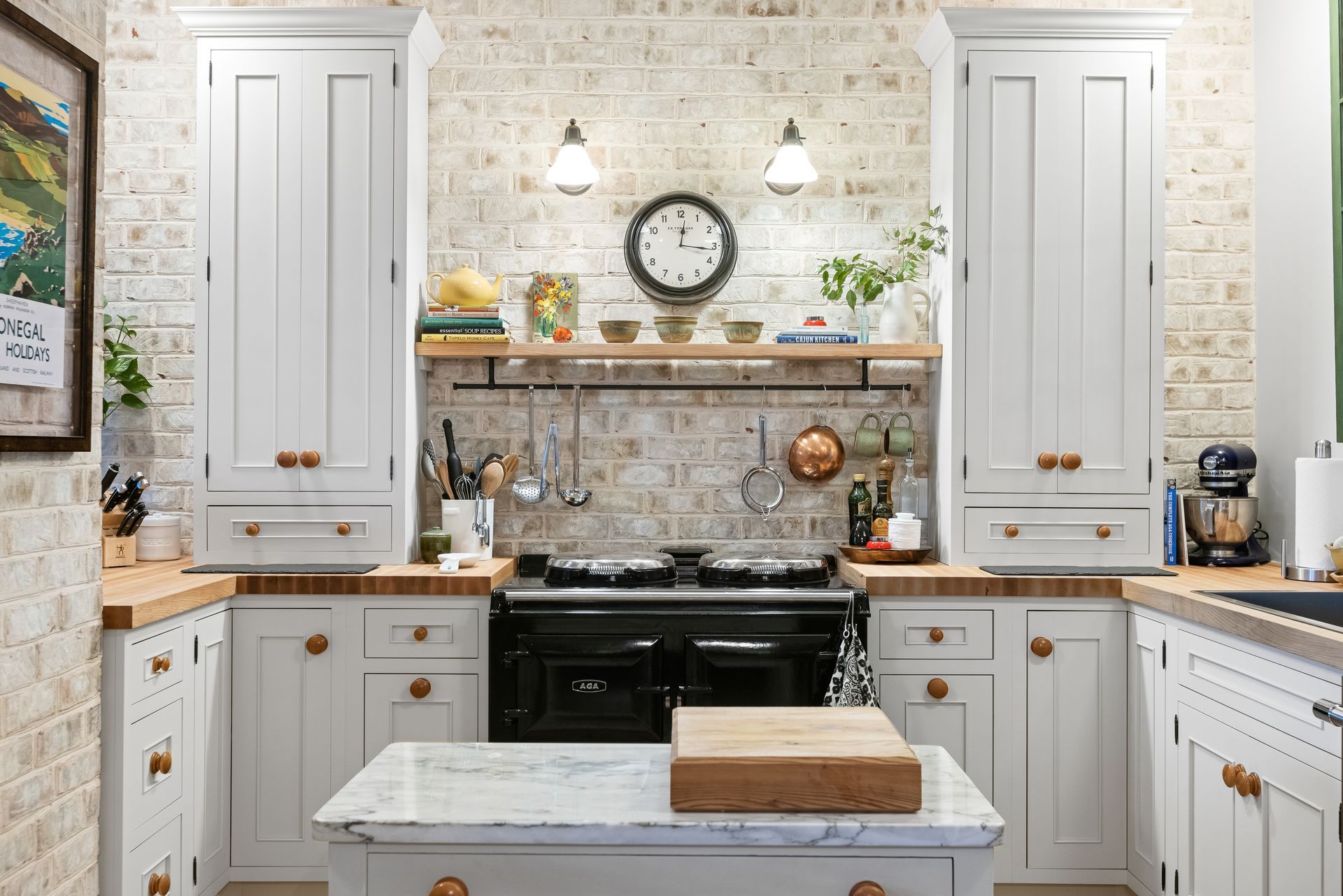 White kitchen with exposed brick, black stove, island, clock, wooden countertops, and white cabinets.