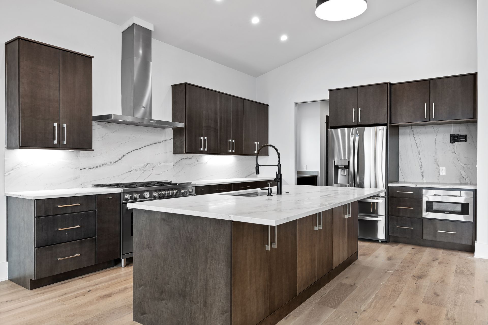 Modern kitchen with dark wood cabinets, white countertops, and stainless steel appliances.