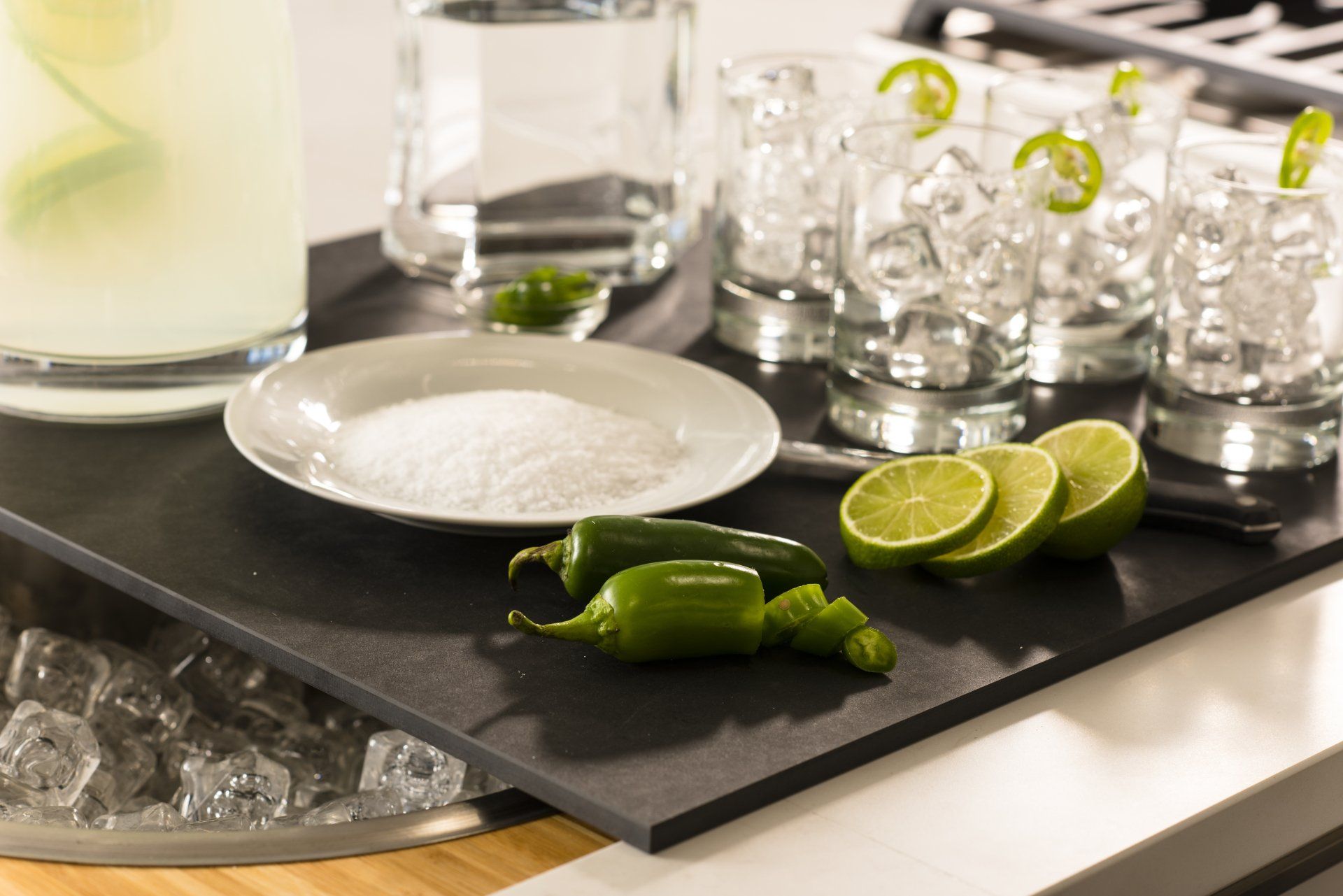 A tray with a plate of salt , limes , jalapenos and shot glasses on it.
