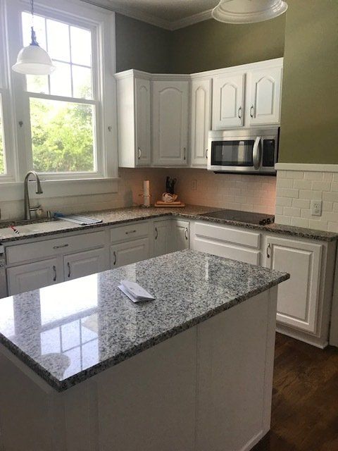 Modern kitchen with white cabinets, granite countertops, stainless steel microwave, and large window providing natural light.