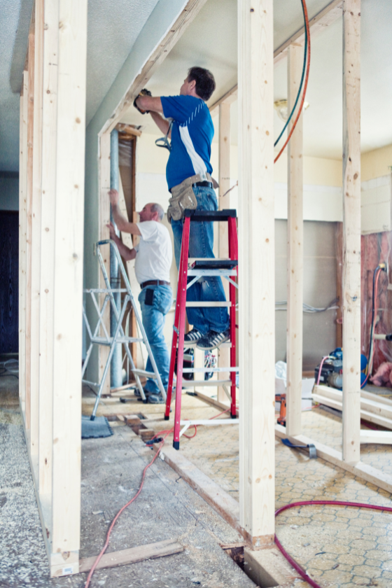 Two men are working on a wooden frame in a room.