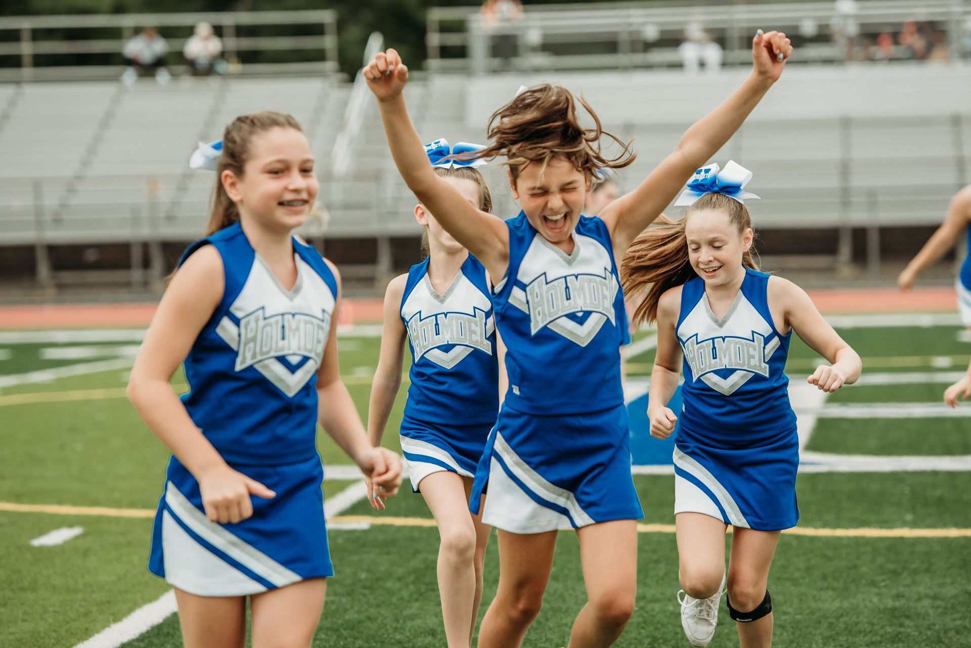 Football players in action on a grassy field; one runs with the ball, pursued by two opponents.