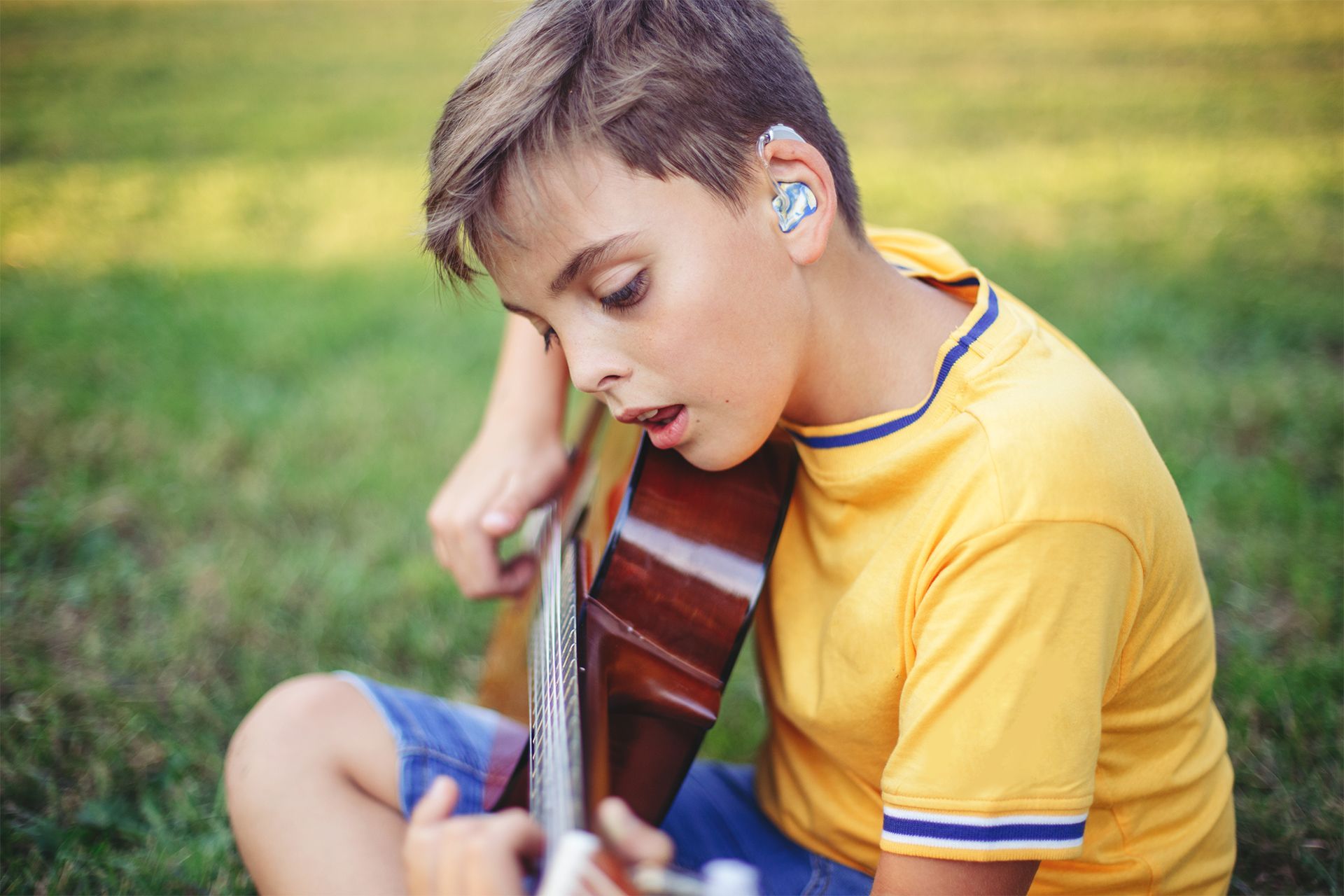Little Boy With Hearing Aid Playing Guitar