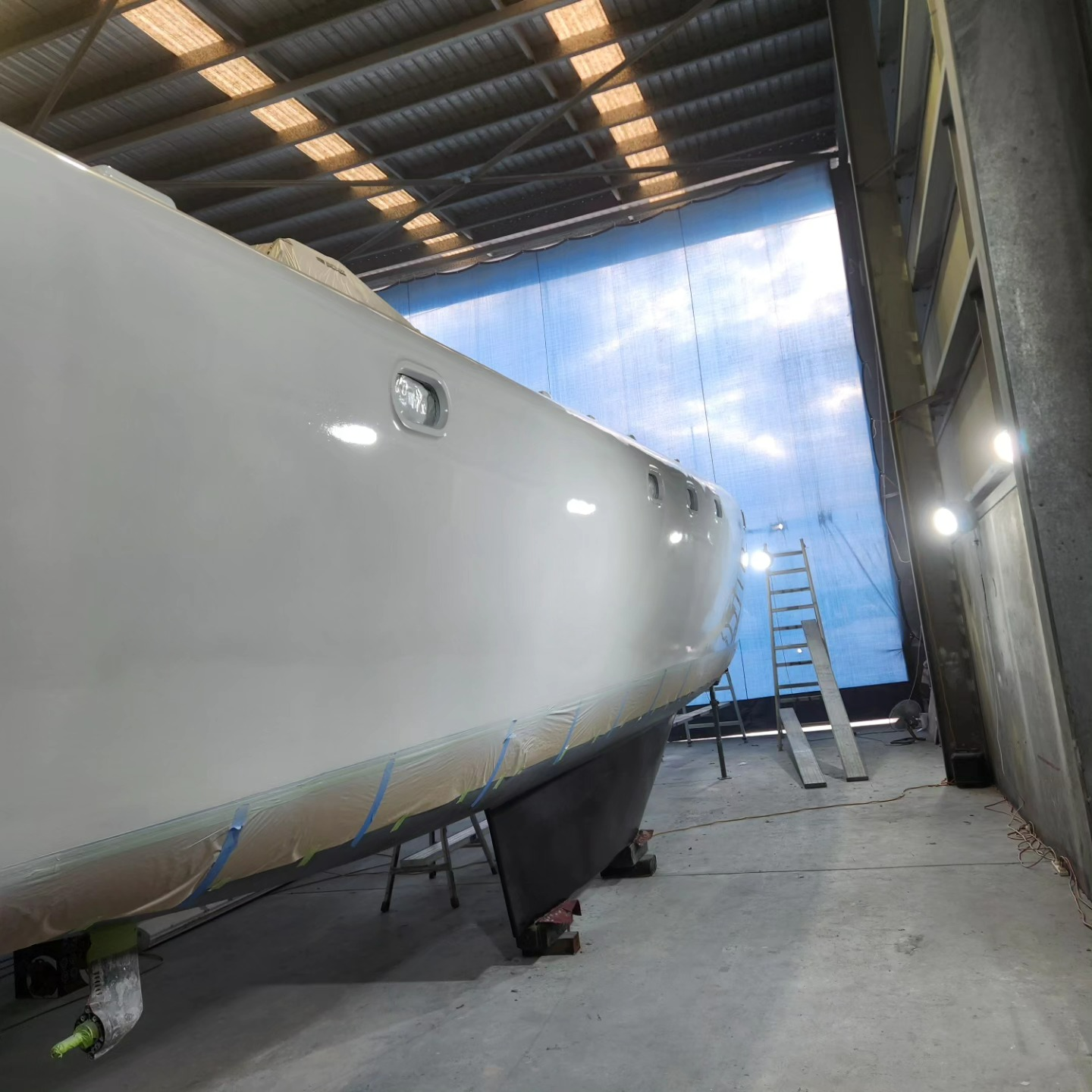 A Boat is Being Painted in a Garage With a Blue Curtain Behind It — Baran Yachting in Coomera, QLD