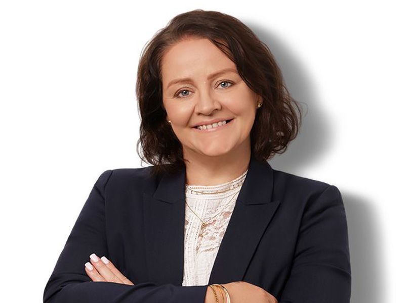 A woman with short brown hair is smiling and wearing a black jacket.