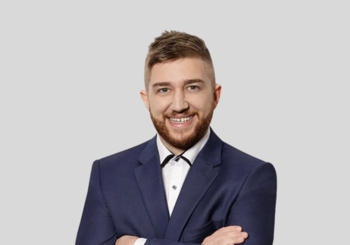 A man in a suit and bow tie is smiling with his arms crossed.